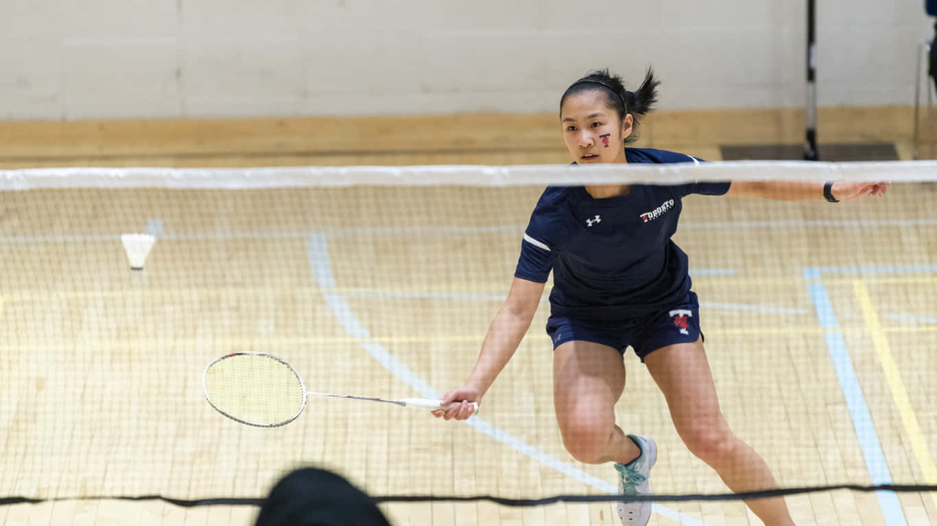 1366x768 Badminton 桌布 壁紙 — 一位專注的女羽毛球選手在室內場地揮拍時向前猛衝，羽毛球在空中飛翔。