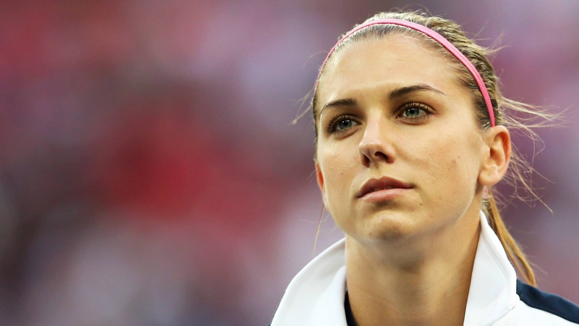 Alex Morgan 桌布 壁紙 — 一位專注的女運動員戴著粉紅色頭帶，在日間體育賽事中凝視著。