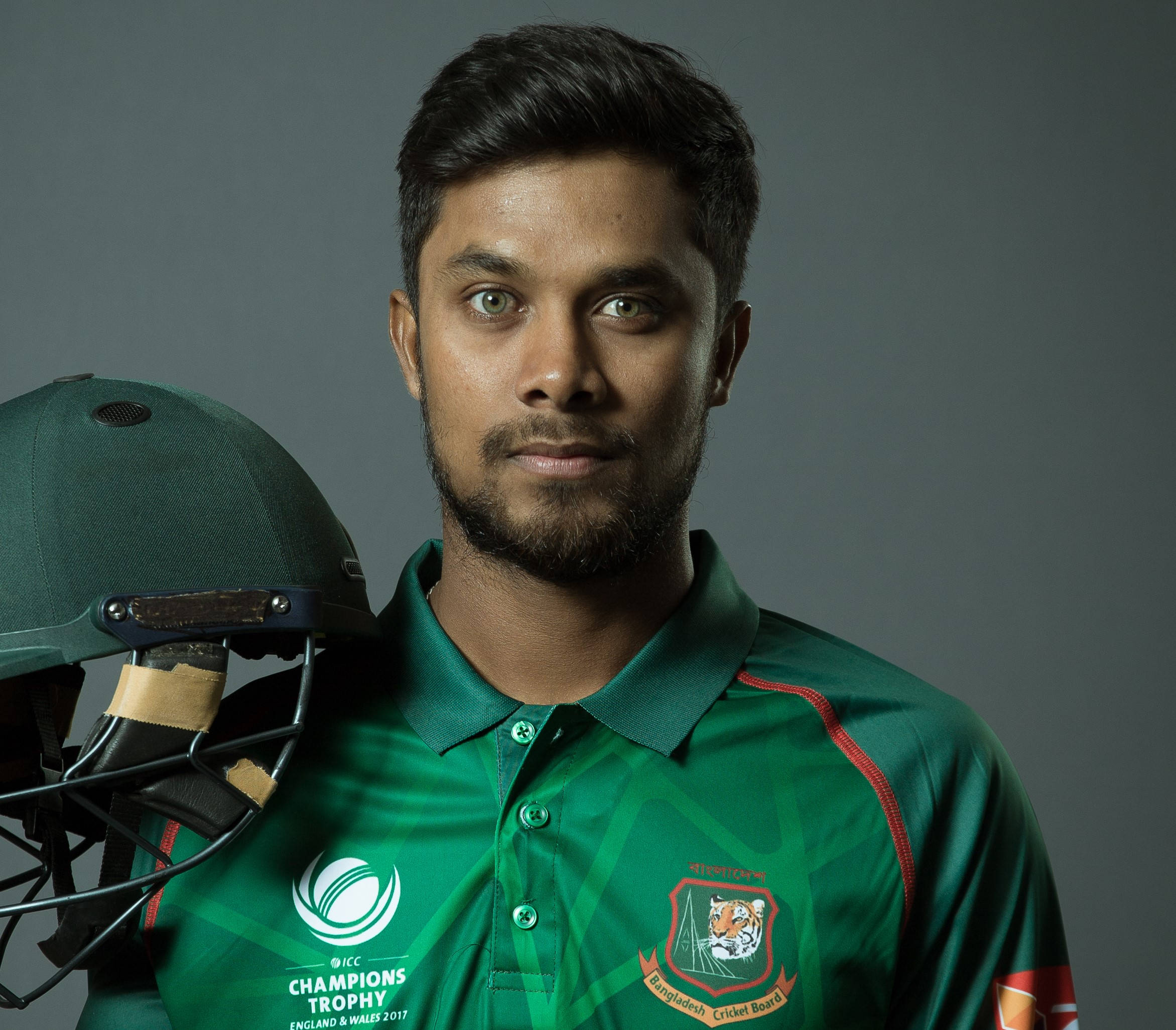 Bangladesh Cricket 桌布 壁紙 — 一位專注的孟加拉國板球運動員穿著綠色制服，在灰色中性攝影棚背景前手持頭盔。