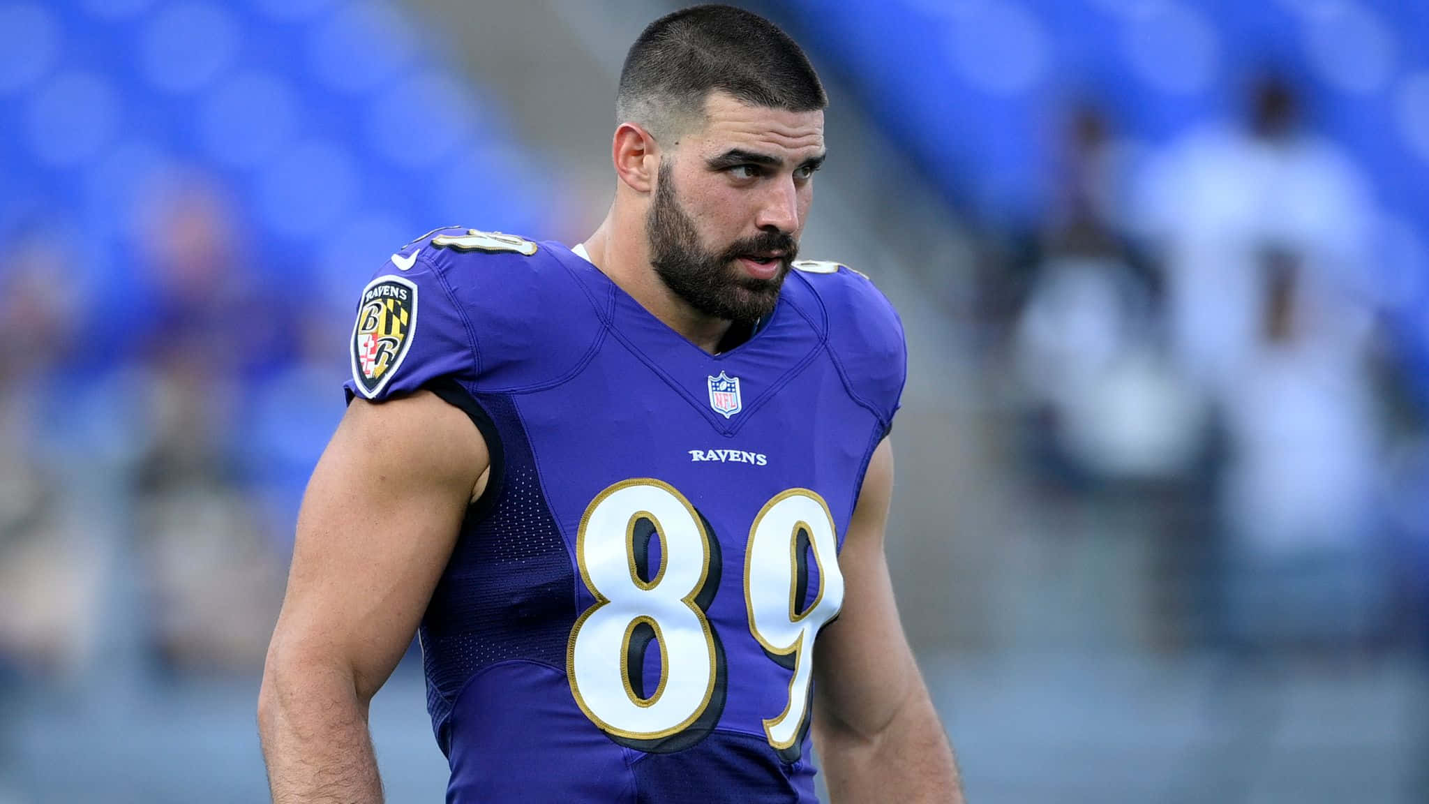 Mark Andrews 桌布 壁紙 — 一位專注的巴爾的摩烏鴉隊美式足球員，身穿紫色89號球衣，站在球場上，背景的體育場座位模糊不清。