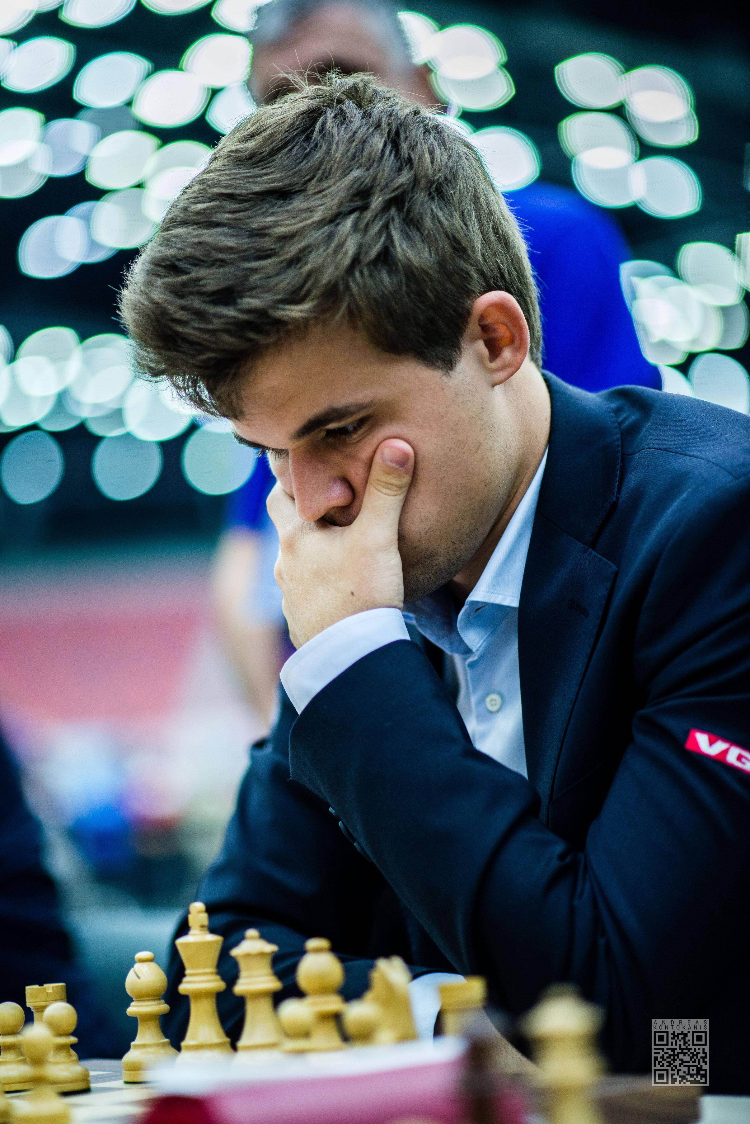Magnus 桌布 壁紙 — 一位專注的年輕男子穿著西裝，在比賽中俯身於棋盤上，手托著臉，陷入沉思。