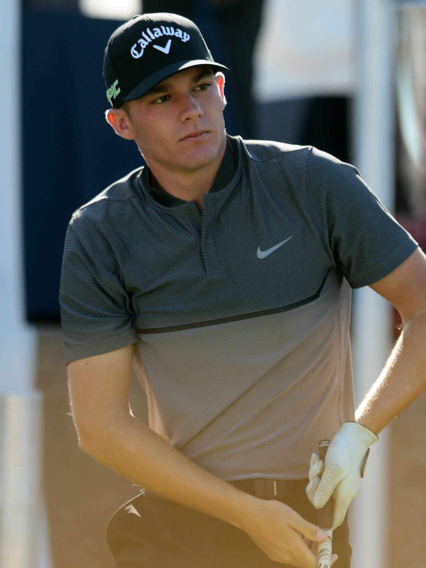 Nike 桌布 壁紙 — 一位專注的年輕男性高爾夫球手，戴著 Callaway 帽子和 Nike 馬球衫，在明亮的日光下堅定地握著球桿。