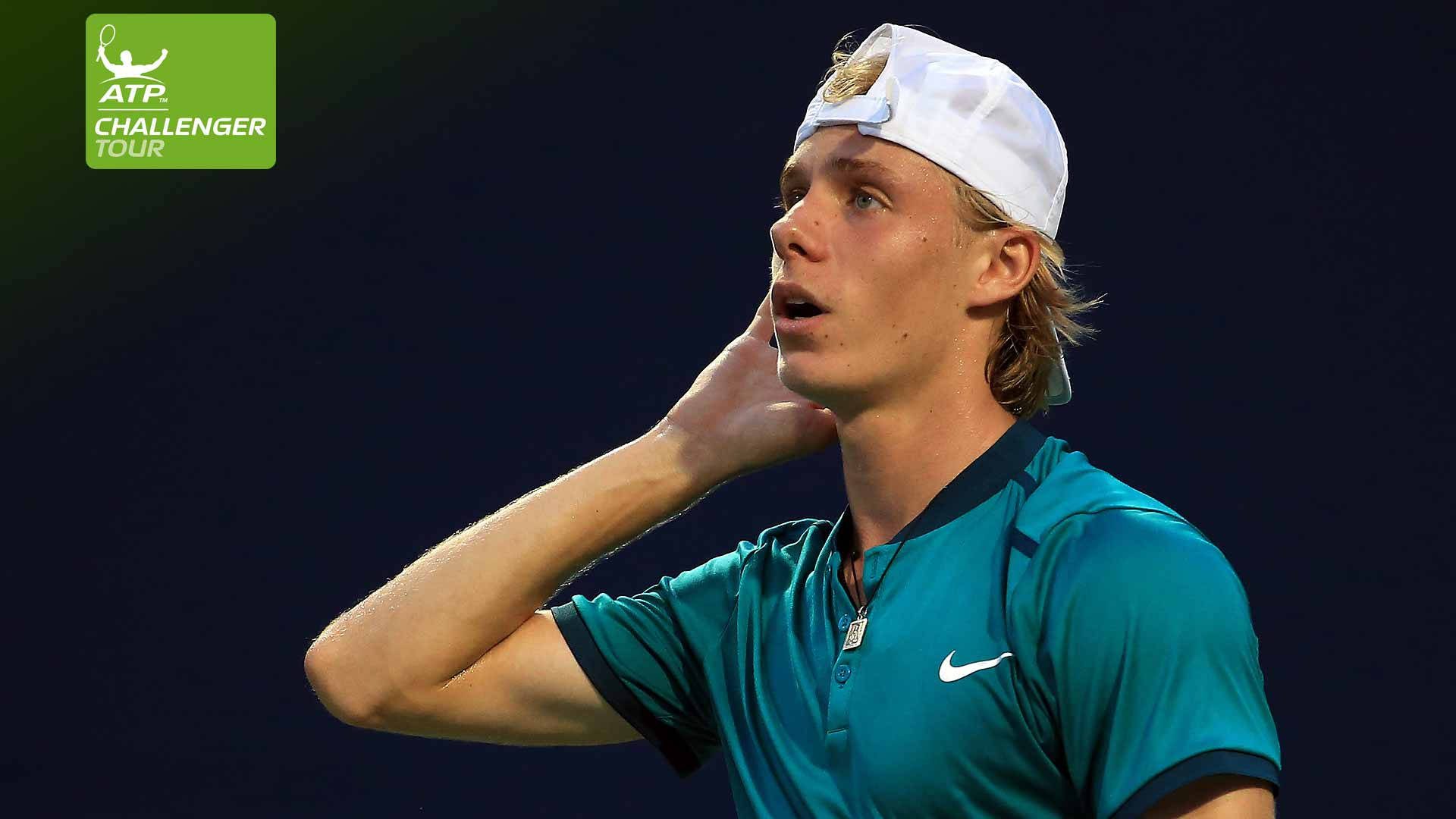 Denis 桌布 壁紙 — 一位專注的年輕男網球選手，身穿青綠色襯衫和白色帽子，在明亮的體育場燈光下的一場夜間比賽中觸摸他的脖子。