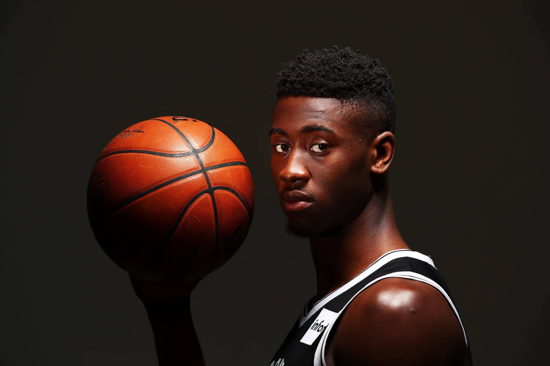 caris levert 桌布 壁紙 — 一位專注的年輕籃球運動員身穿黑白球衣，在深色攝影棚背景前手持橙色籃球。