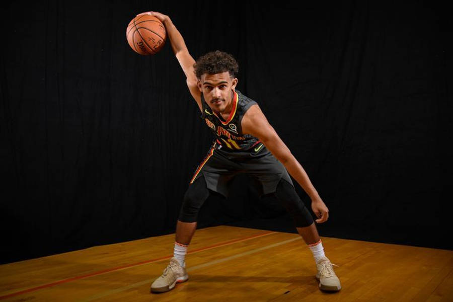 Trae Young 桌布 壁紙 — 一位專注的年輕籃球運動員身穿黑色球衣，在木質球場上對著深色攝影棚背景準備投籃。