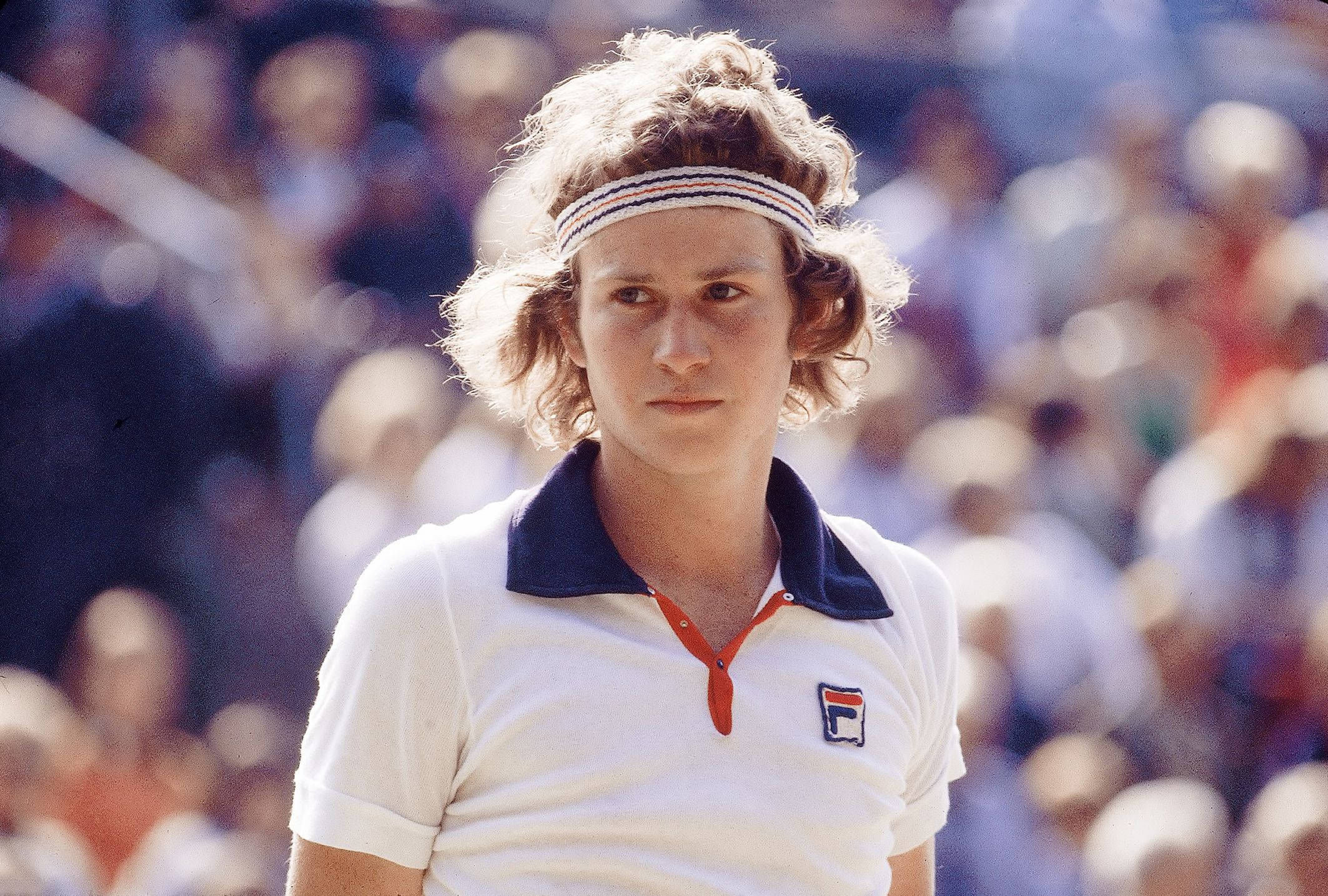 Tennis 桌布 壁紙 — 一位專注的年輕網球運動員，留著捲髮並戴著頭帶，在明亮的日光下比賽時專注地凝視。