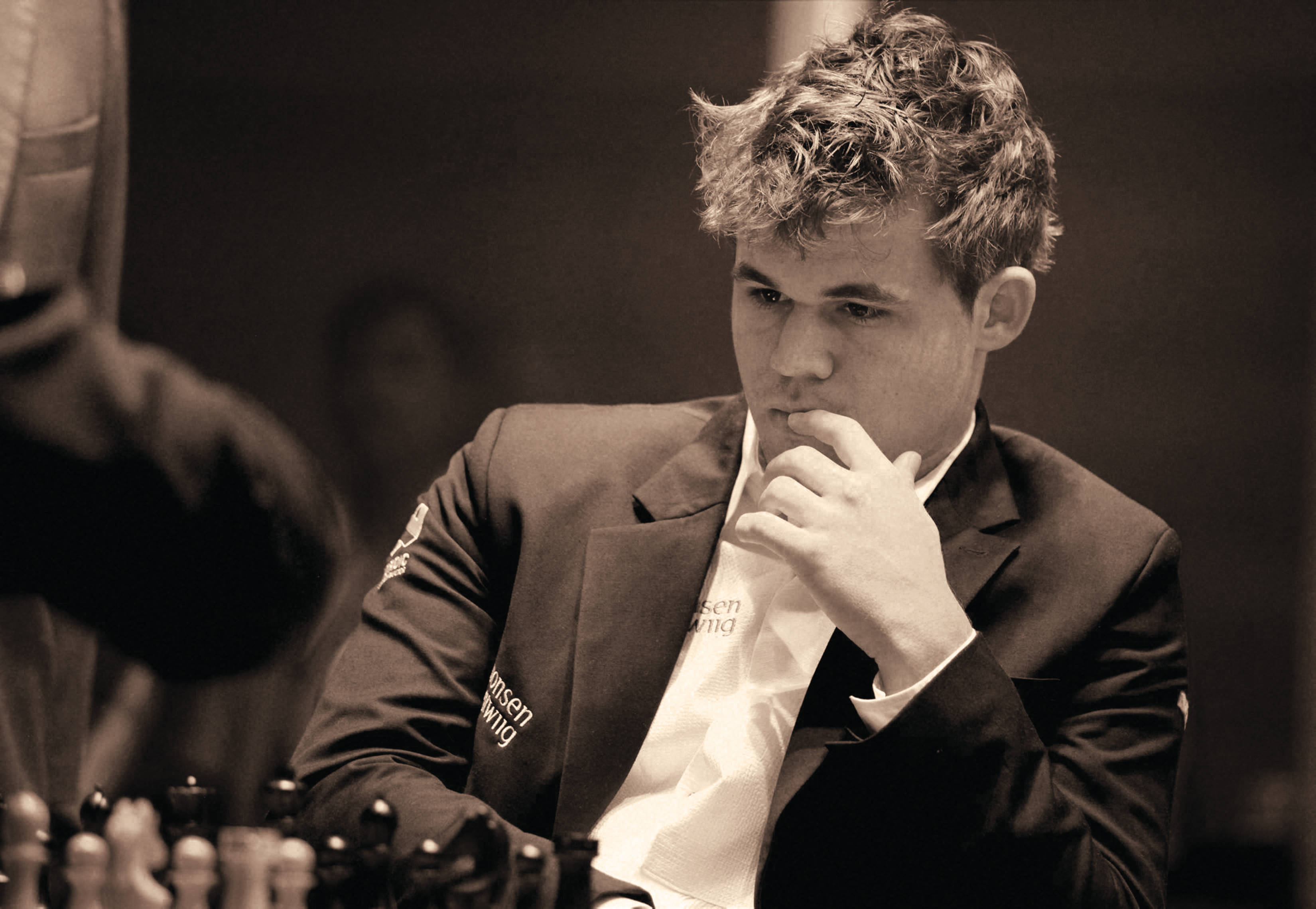 Magnus 桌布 壁紙 — 一位專注的年輕西洋棋選手穿著西裝，在比賽中手托下巴思考下一步棋。