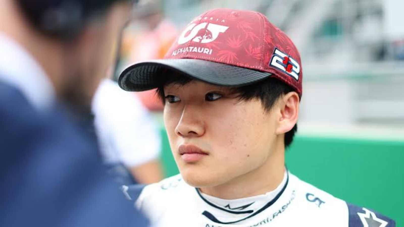 Racing 桌布 壁紙 — 一位專注的年輕賽車手，戴著AlphaTauri帽子和賽車服，在維修站期間專注地看著隊友。