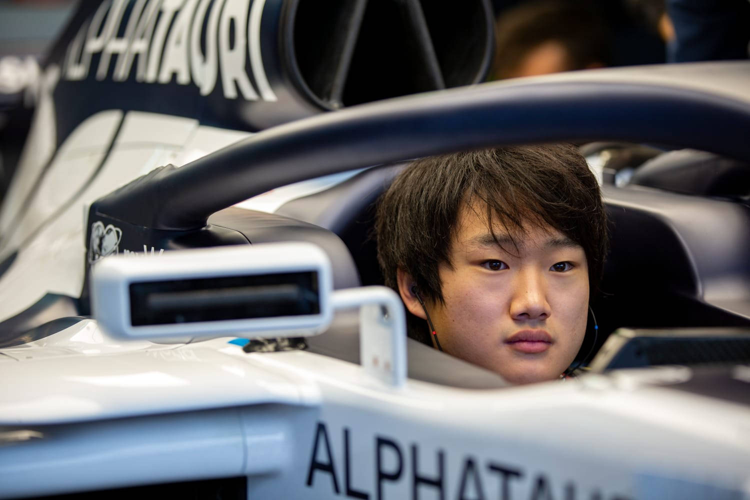 Racing 桌布 壁紙 — 一位專注的年輕車手從流線型白色AlphaTauri一級方程式賽車駕駛艙內凝視著。