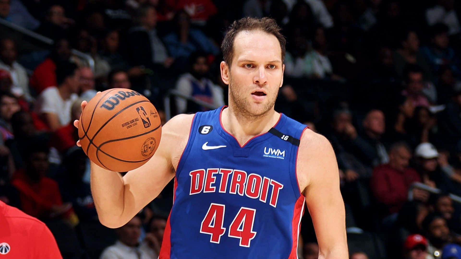 NBA 桌布 壁紙 — 一位專注的底特律活塞籃球運動員，身穿藍色球衣44號，在比賽中手持籃球，背景是模糊的人群。