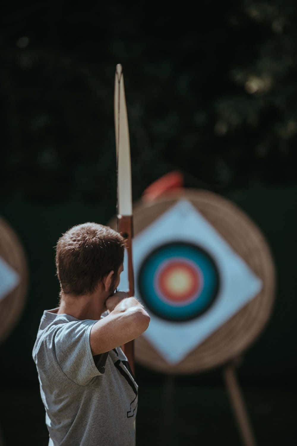 Archery 桌布 壁紙 — 一位專注的弓箭手拉弓瞄準一個色彩繽紛的目標，背景是深色樹葉。