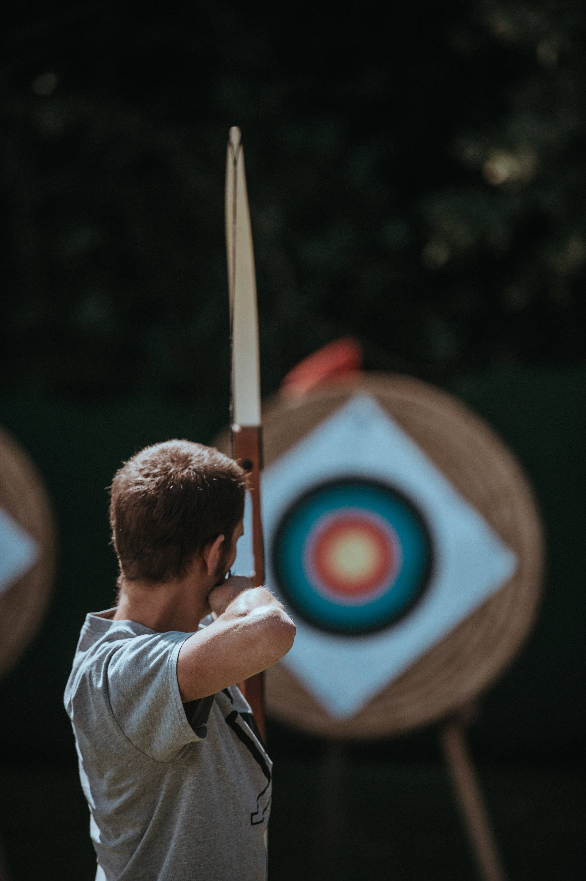 Archery 桌布 壁紙 — 一位專注的弓箭手拉弓瞄準色彩繽紛的靶心，背景是模糊的綠色植物。