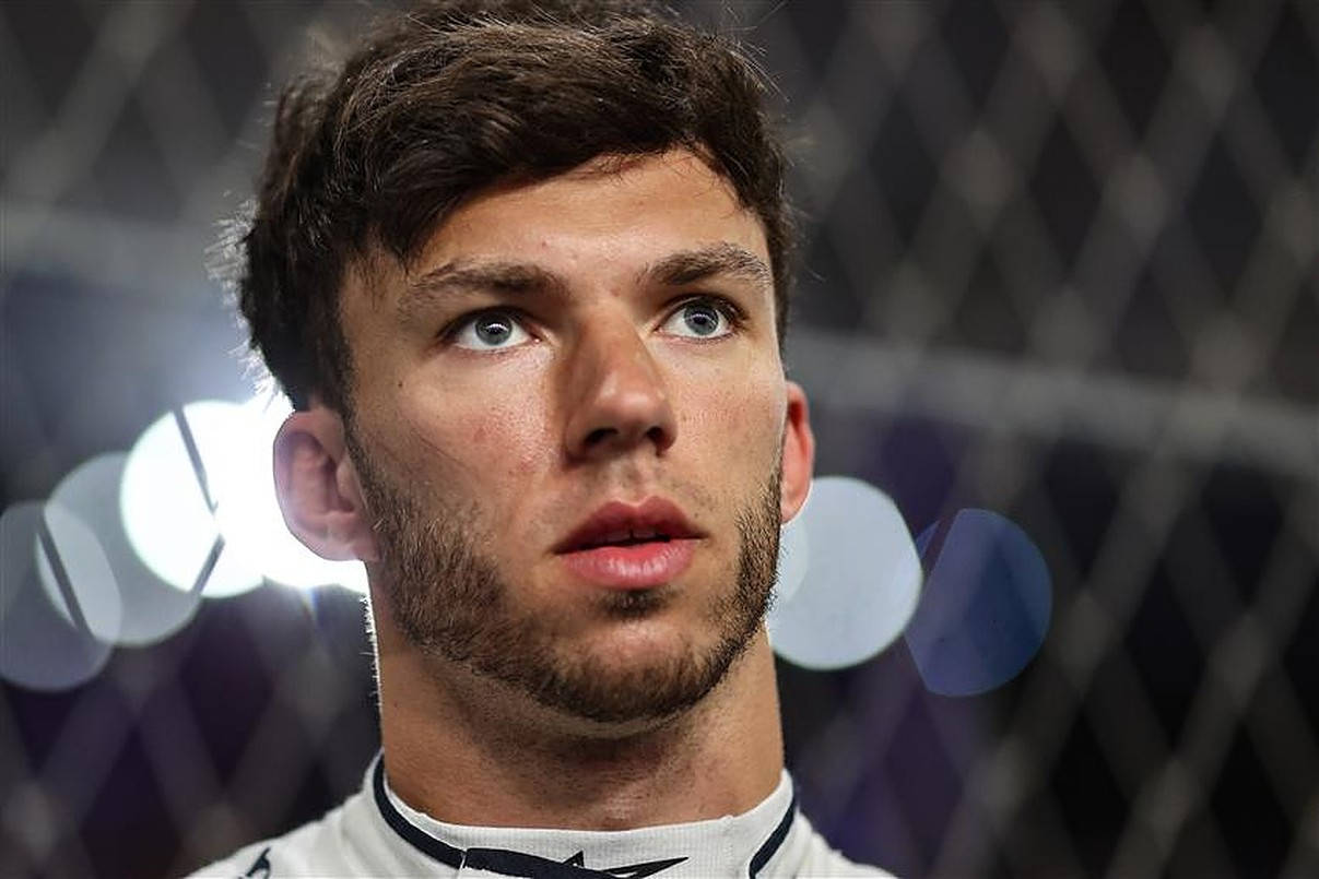 pierre gasly 桌布 壁紙 — 一位專注的戰士，擁有強烈的藍色眼睛，在明亮的體育場燈光下，透過鐵絲網向上凝視。