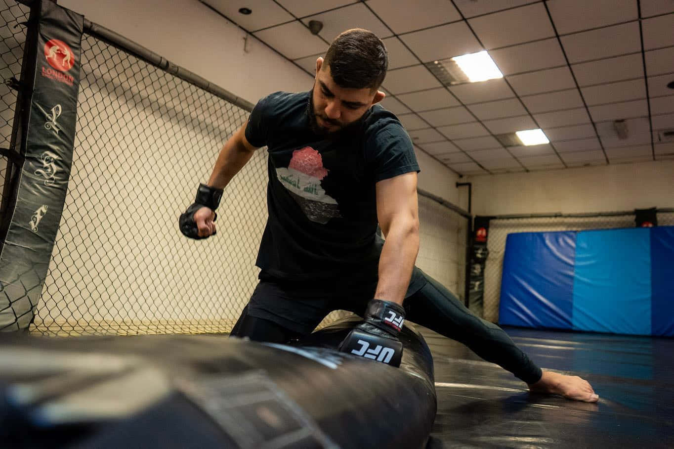 Fitness 桌布 壁紙 — 一位專注的拳手在健身房的籠內，在明亮的頭頂燈光下，對著重沙袋進行激烈訓練。