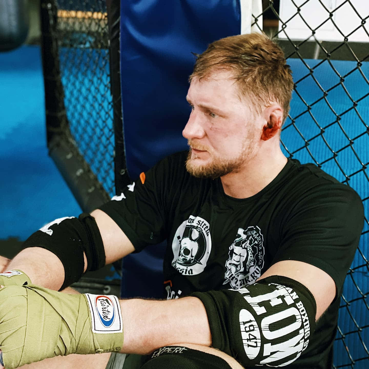 Athletic 桌布 壁紙 — 一位專注的拳手纏著繃帶，在藍色MMA籠內休息，展現決心和毅力。