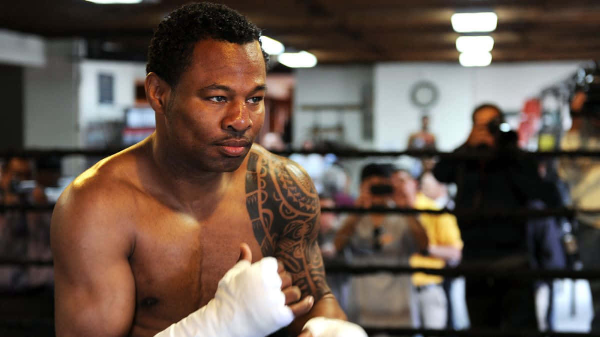 Boxing 桌布 壁紙 — 一位專注的拳擊手，手臂上有刺青，在訓練時戴著白色手套站在擂台上。