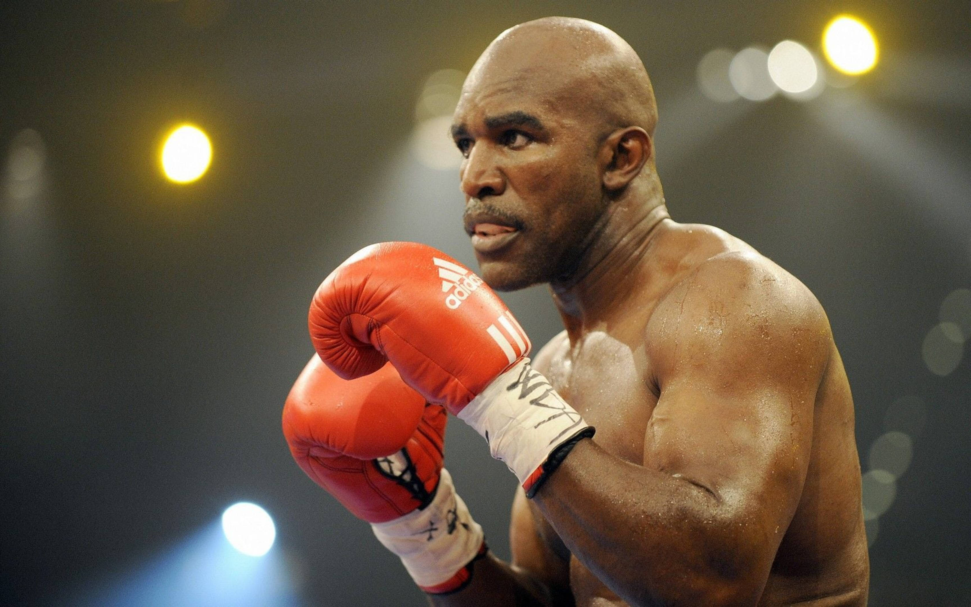 Boxing 桌布 壁紙 — 一位專注的拳擊手戴著紅色手套，在昏暗的擂台上準備就緒，頭頂是明亮的聚光燈。