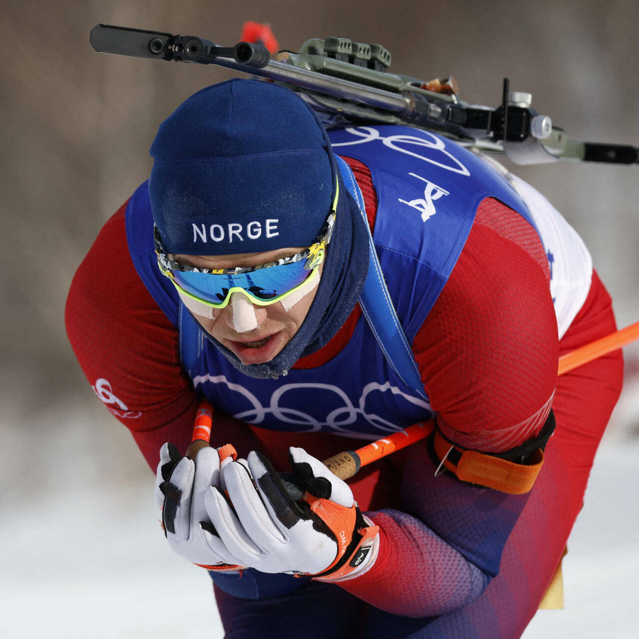 運動 桌布 壁紙 — 一位專注的挪威冬季兩項運動員，身穿紅藍裝備，背著步槍在雪地中衝刺。