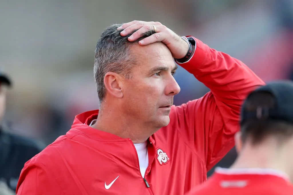 Urban Meyer 桌布 壁紙 — 一位專注的教練穿著紅色外套，在體育賽事中將手放在頭上。