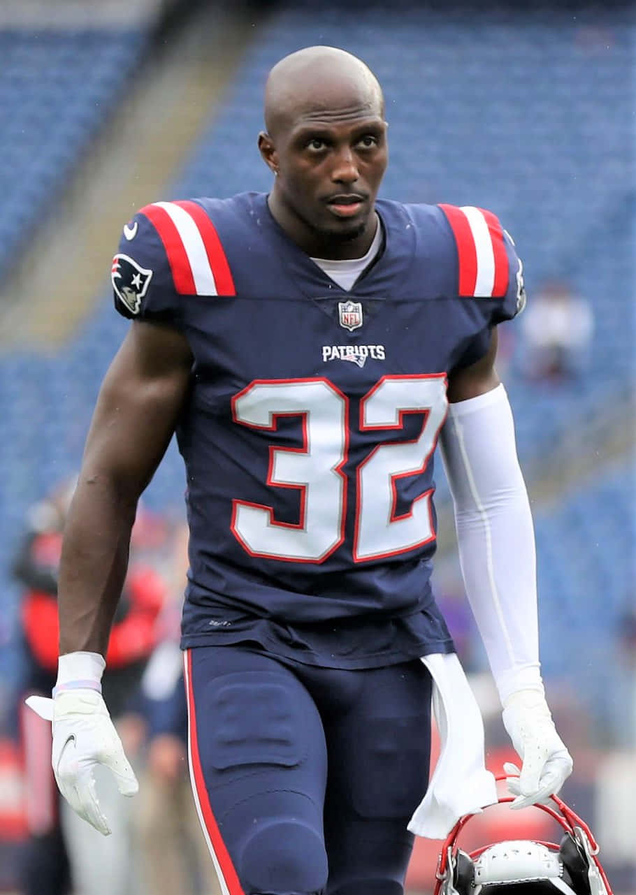 Devin Mccourty 桌布 壁紙 — 一位專注的新英格蘭愛國者隊美式足球員（32號）拿著頭盔在球場上行走。