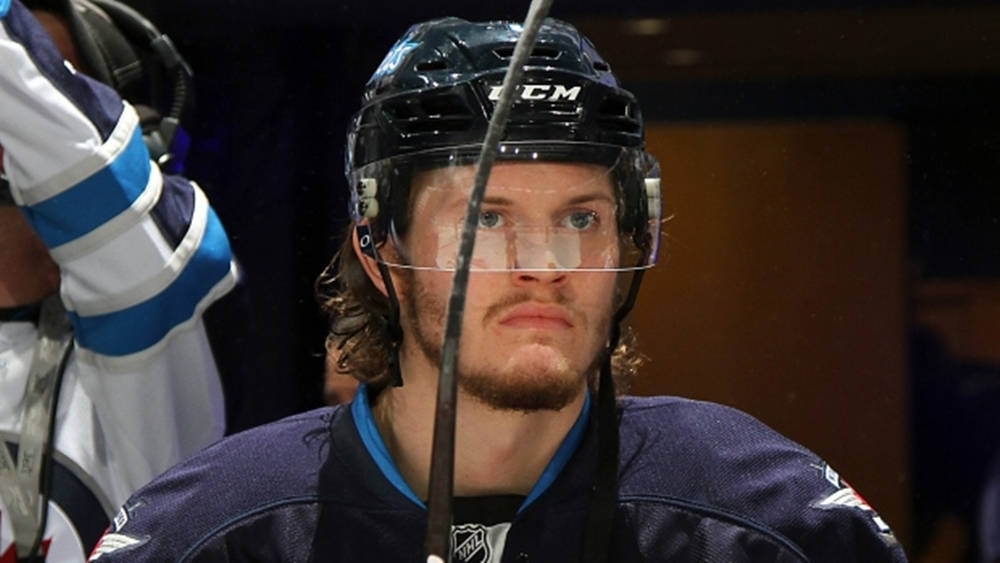 hockey 桌布 壁紙 — 一位專注的曲棍球運動員，身穿深藍色球衣和黑色頭盔，在昏暗的場館中凝視著，同時握著他的球桿。