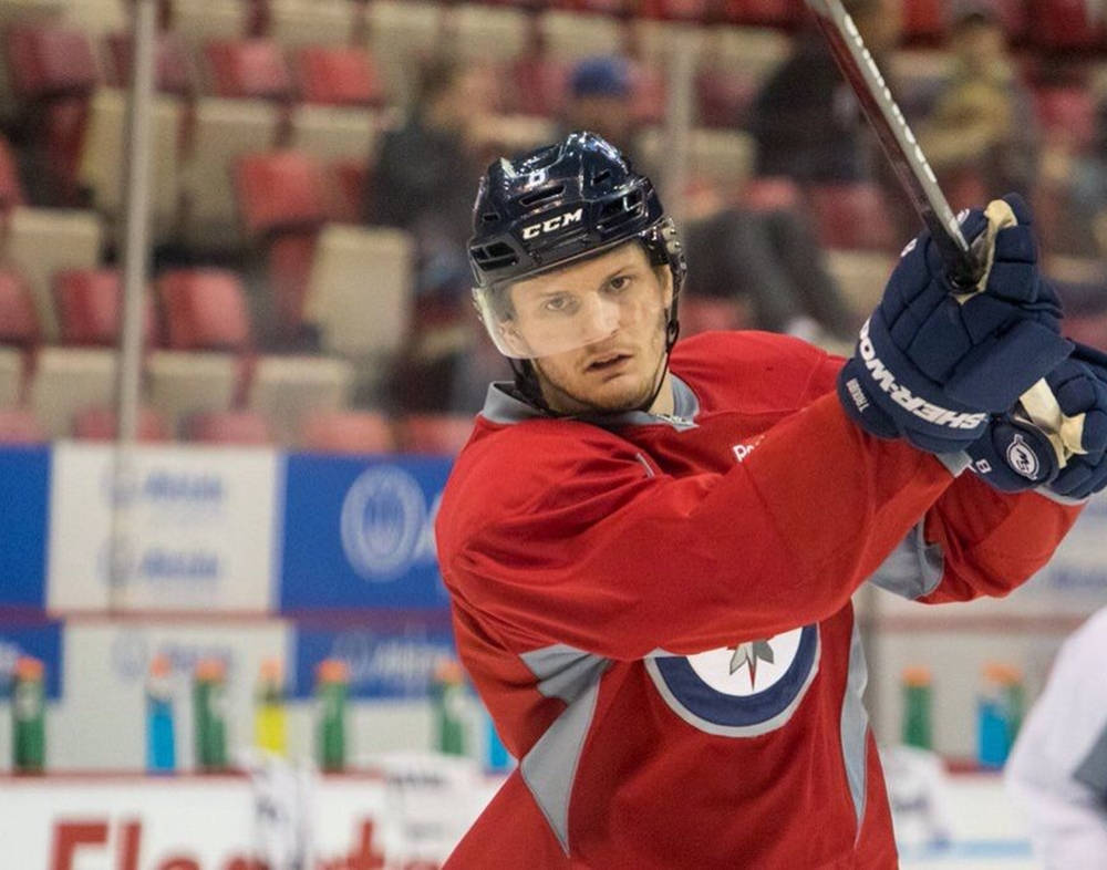 hockey 桌布 壁紙 — 一位專注的曲棍球運動員穿著紅色球衣在冰場上揮動球桿，背景是模糊的體育館座位。