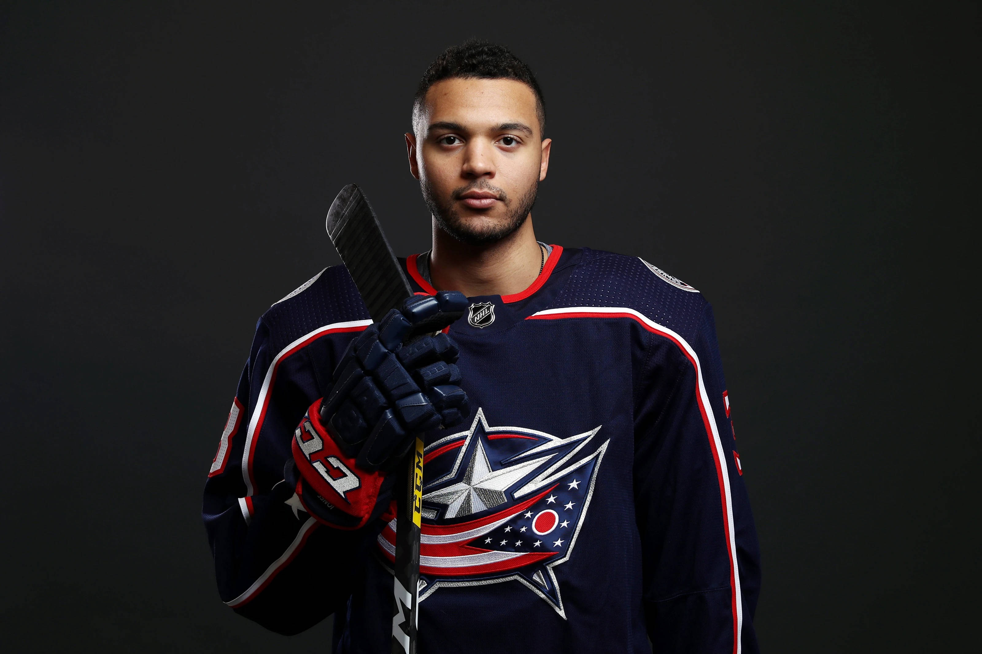 hockey 桌布 壁紙 — 一位專注的曲棍球運動員身穿哥倫布藍夾克球衣，在深色攝影棚背景下握著球桿。