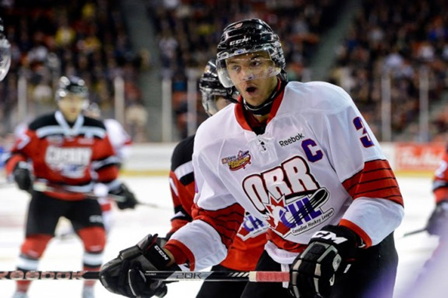 hockey 桌布 壁紙 — 一位專注的曲棍球運動員身穿白色和紅色球衣，帶有隊長 'C' 標誌，在冰上激烈的比賽中大喊。