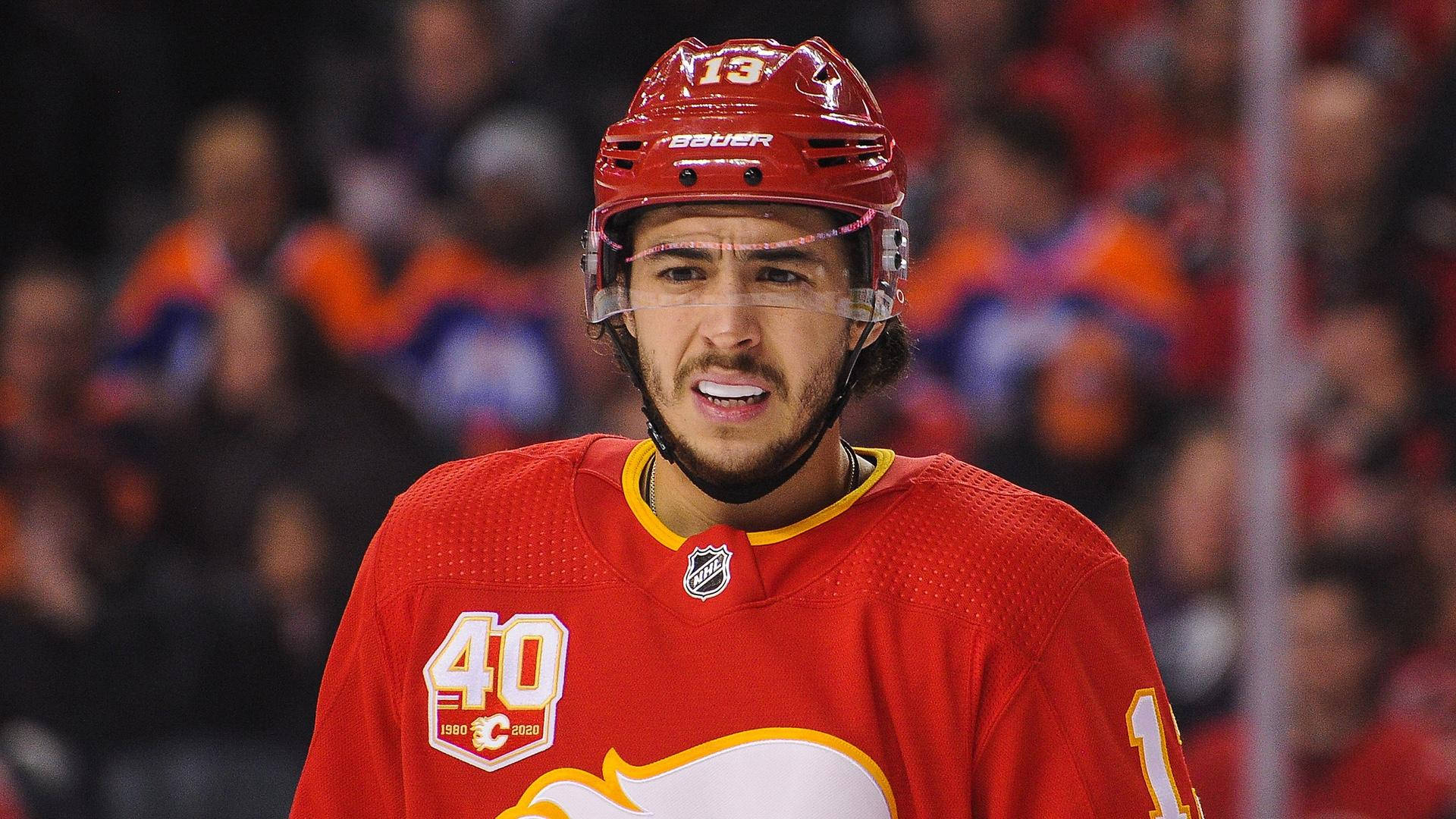 Johnny Gaudreau 桌布 壁紙 — 一位專注的曲棍球運動員身穿紅色球衣和頭盔，帶著堅定的表情站在冰上。