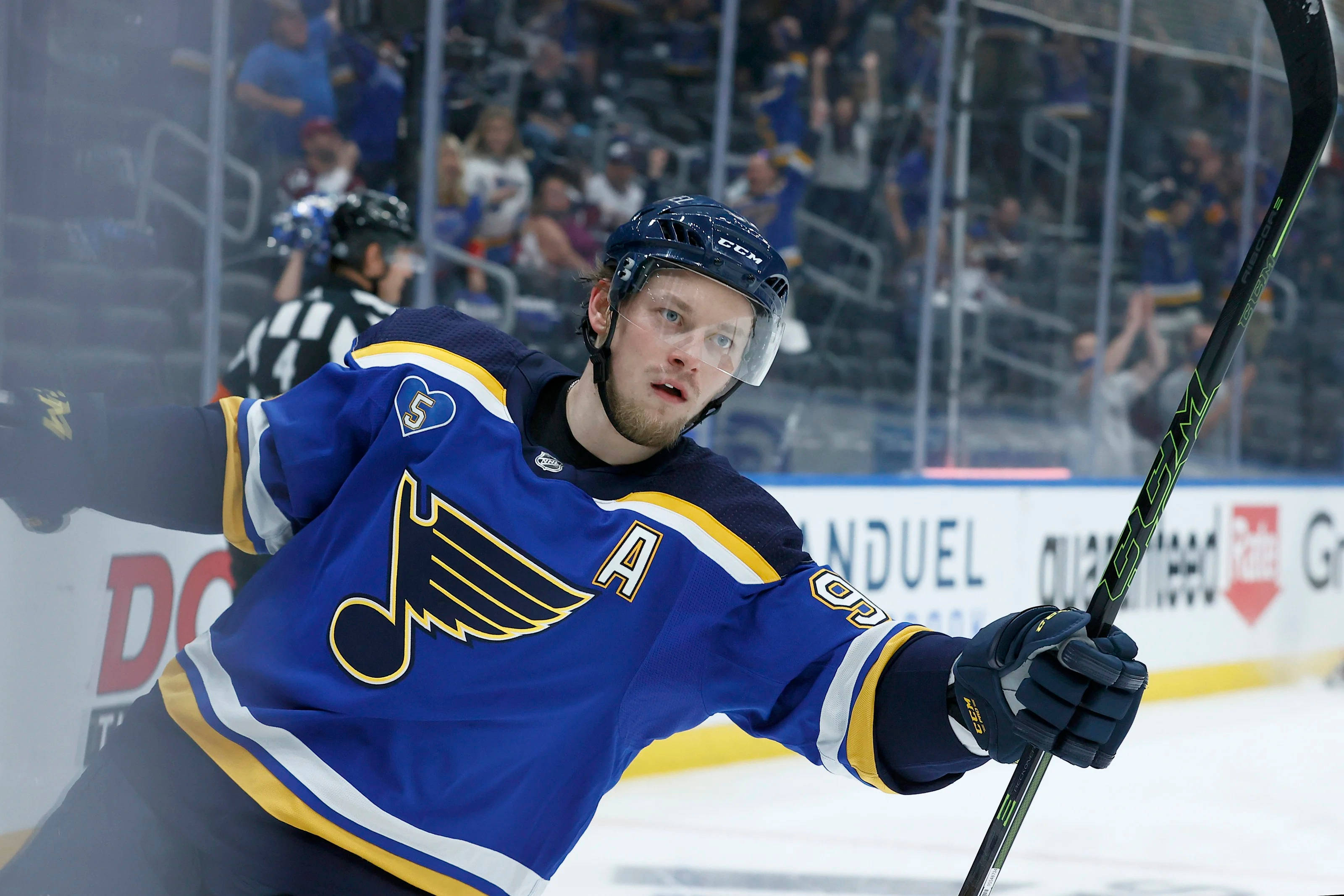 St Louis Blues 桌布 壁紙 — 一位專注的曲棍球運動員身穿藍色和金色球衣，在冰上向前傾，手持球棍進行比賽。
