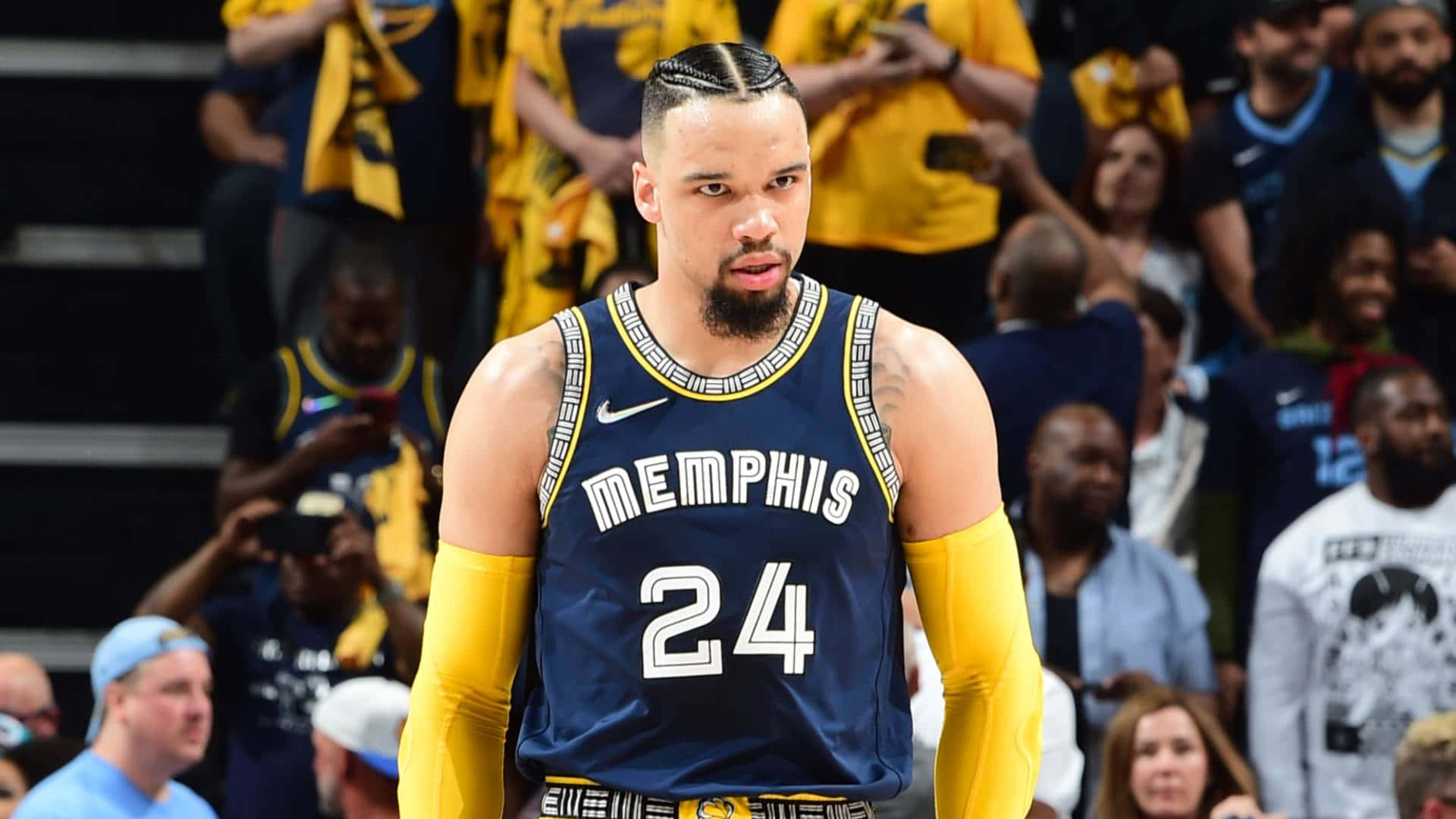 Dillon Brooks 桌布 壁紙 — 一位專注的曼菲斯灰熊籃球運動員身穿海軍藍24號球衣，在比賽中戴著黃色護臂站在球場上。