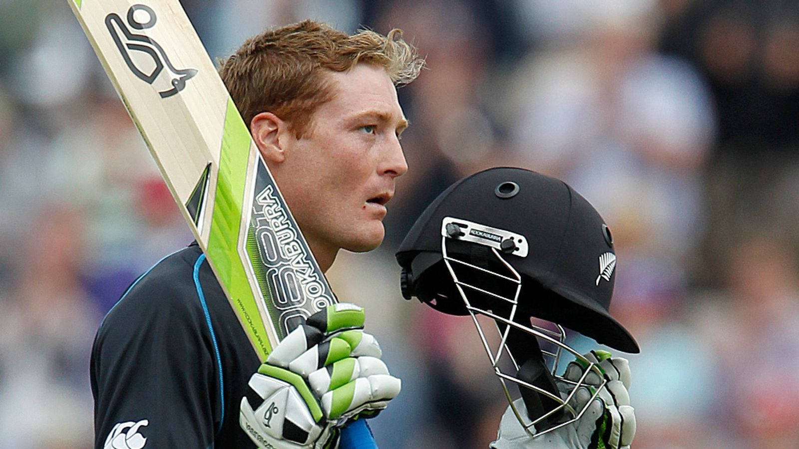 martin guptill 桌布 壁紙 — 一位專注的板球運動員在日間比賽中手持球棒和頭盔，背景有模糊的觀眾。