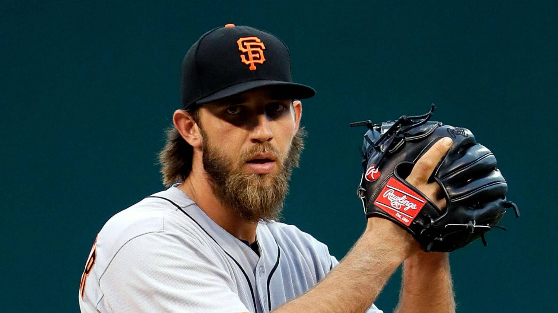 madison bumgarner 桌布 壁紙 — 一位專注的棒球投手，留著鬍鬚，戴著帽子，在深綠色背景下握著手套準備投球。