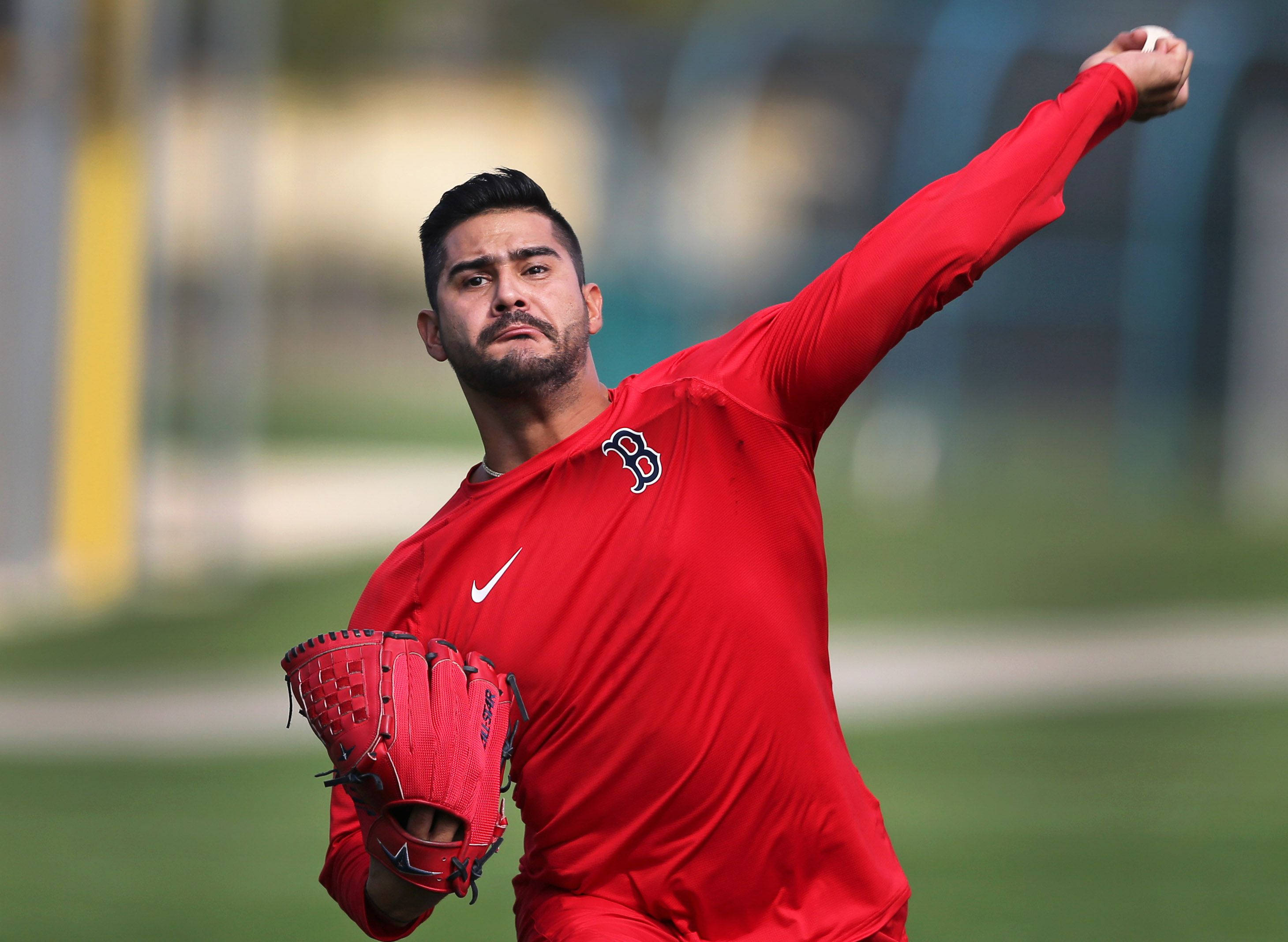 運動 桌布 壁紙 — 一位專注的棒球投手身穿紅色球衣在綠色球場上投球，背景模糊。