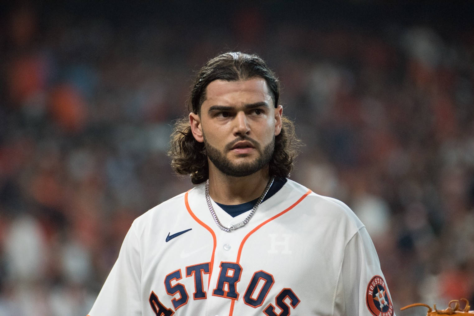Houston Astros 桌布 壁紙 — 一位專注的棒球運動員，留著深色長髮和鬍鬚，在球場燈光下穿著白色太空人隊球衣。