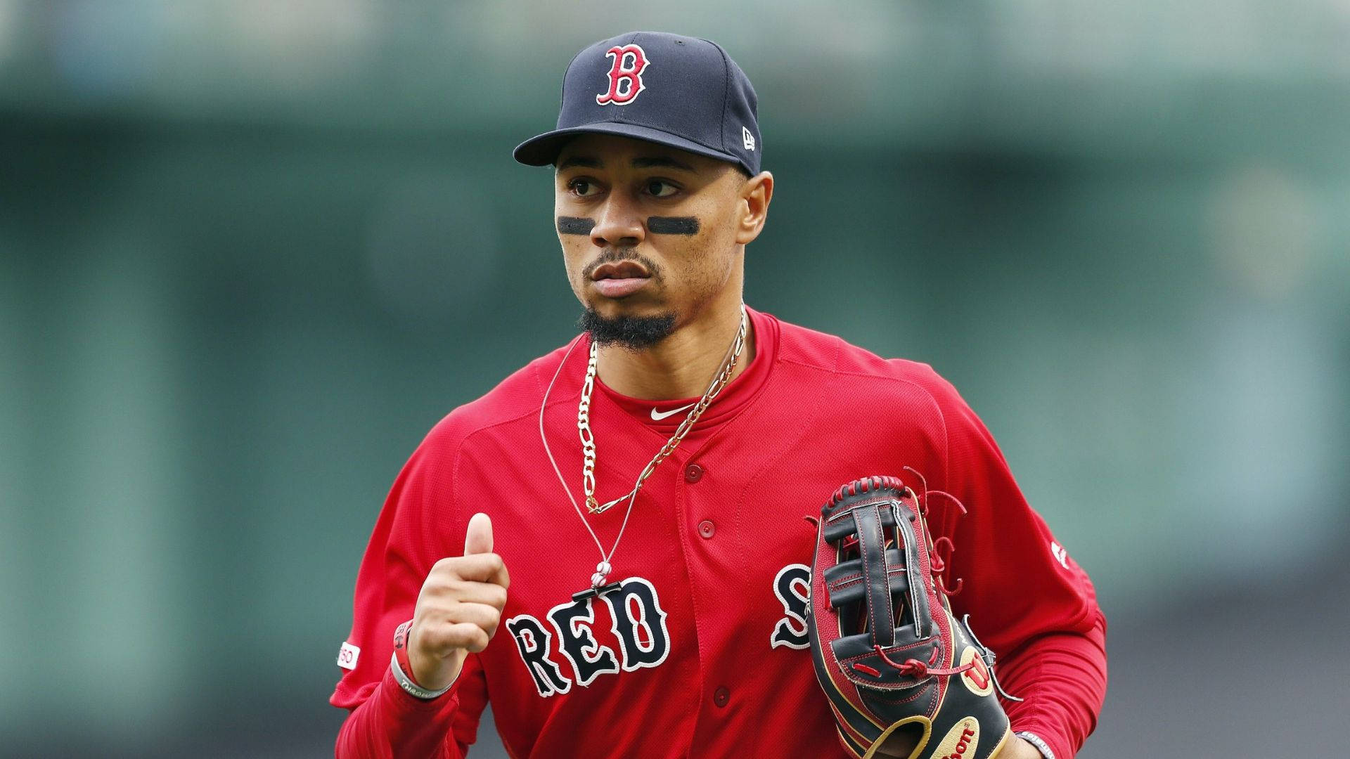 Mookie Betts 桌布 壁紙 — 一位專注的棒球運動員身穿紅色波士頓紅襪隊制服，豎起大拇指，手持手套。