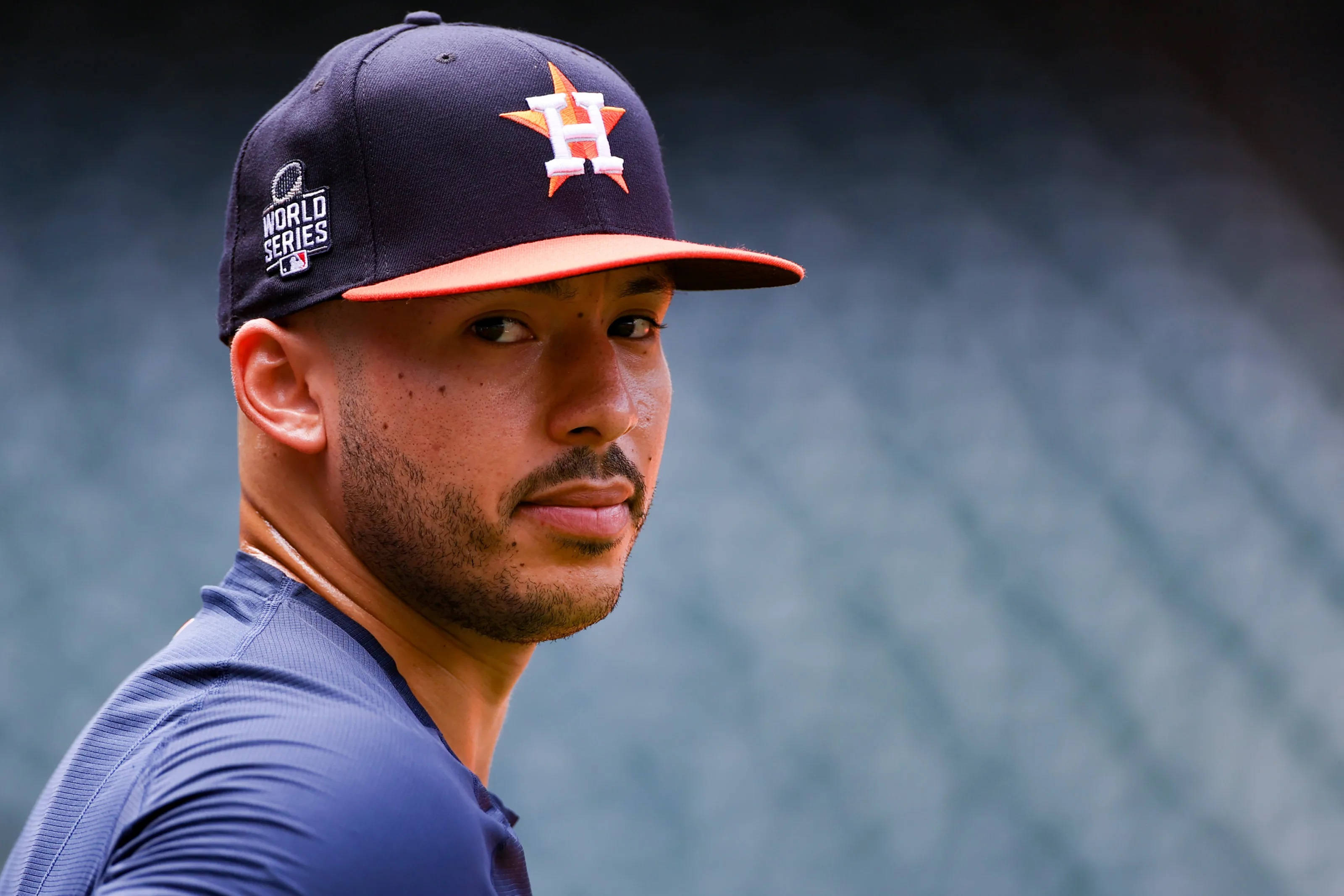 Carlos Correa 桌布 壁紙 — 一位專注的棒球選手戴著休士頓太空人世界大賽帽子，在模糊的球場背景下凝視著。