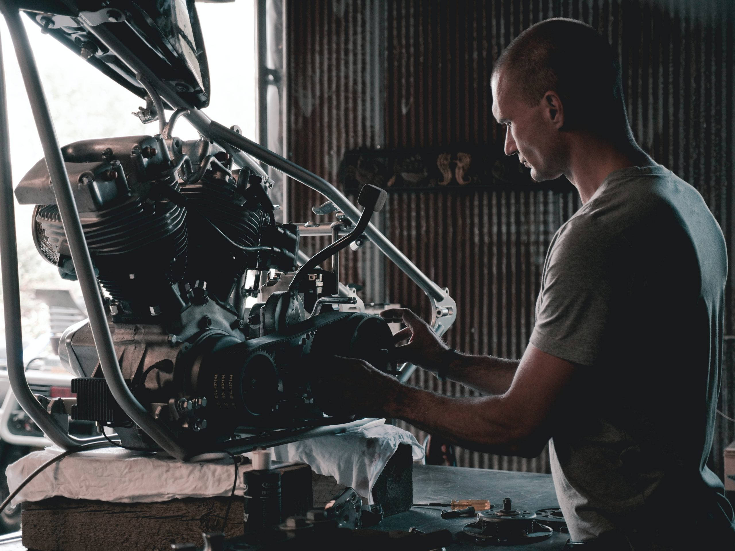 engineering 桌布 壁紙 — 一位專注的機械師在昏暗的車間裡，在自然光下小心地組裝摩托車引擎。