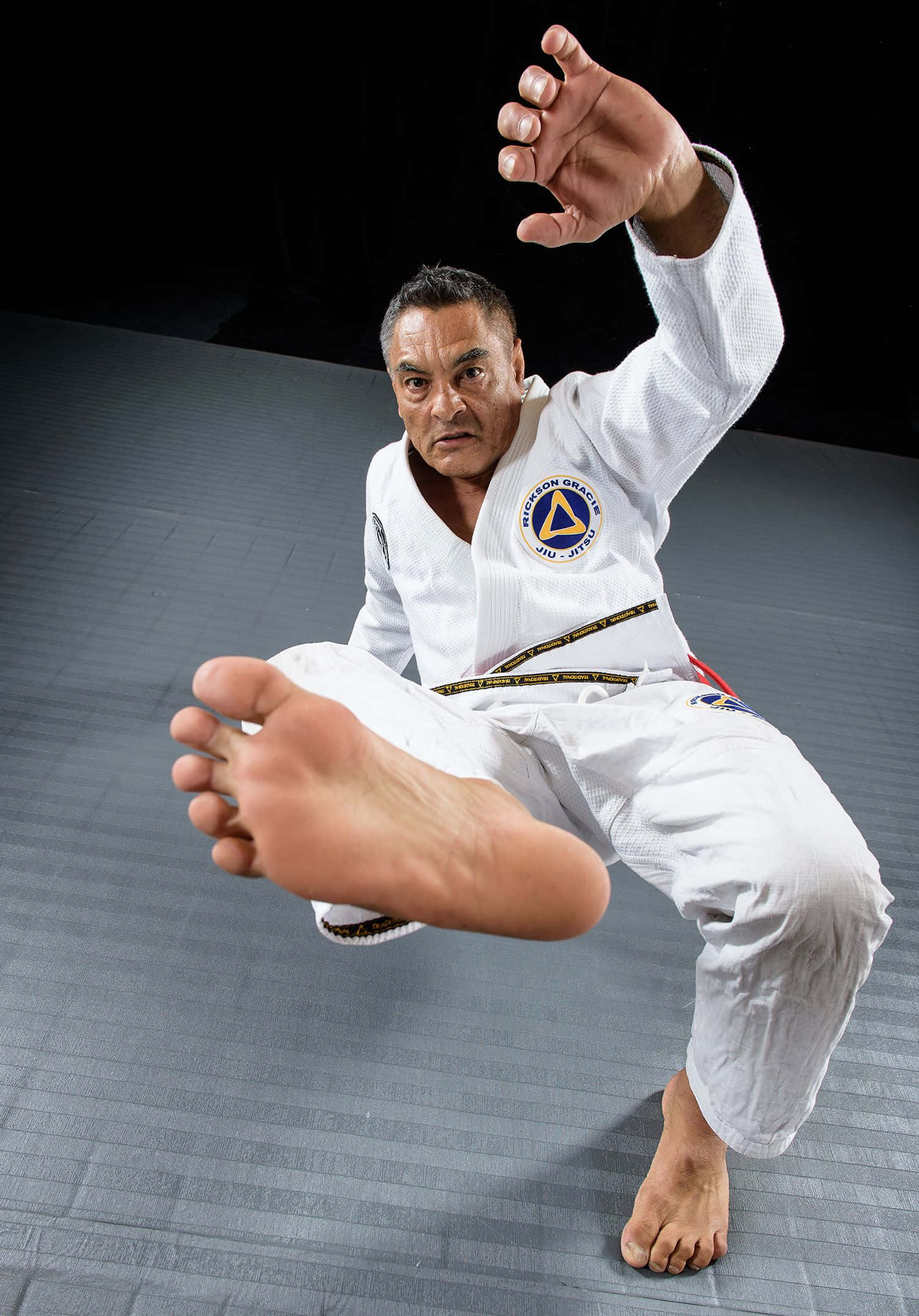 martial arts 桌布 壁紙 — 一位專注的武術家穿著白色道服，在灰色軟墊上對著黑色背景做出一個動態踢腿動作。
