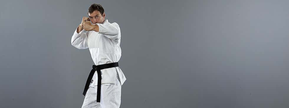 Martial Arts Uniforms 桌布 壁紙 — 一位專注的武術家身穿白色道服，繫著黑帶，在純灰色工作室背景前擺出強而有力的姿勢。