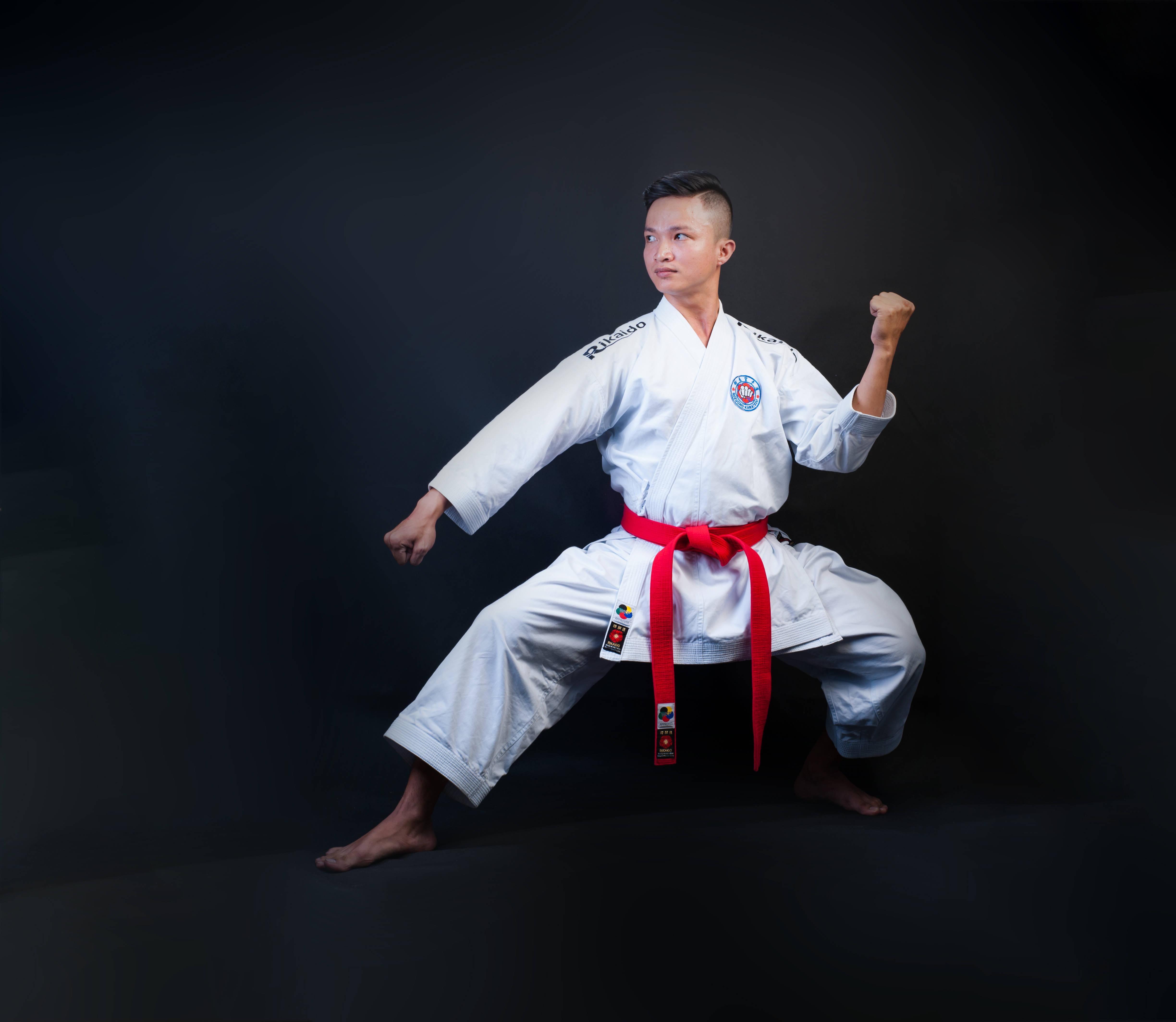 Judo 桌布 壁紙 — 一位專注的武術家身穿白色道服，繫著紅色腰帶，在黑暗的攝影棚背景下擺出強而有力的姿勢。