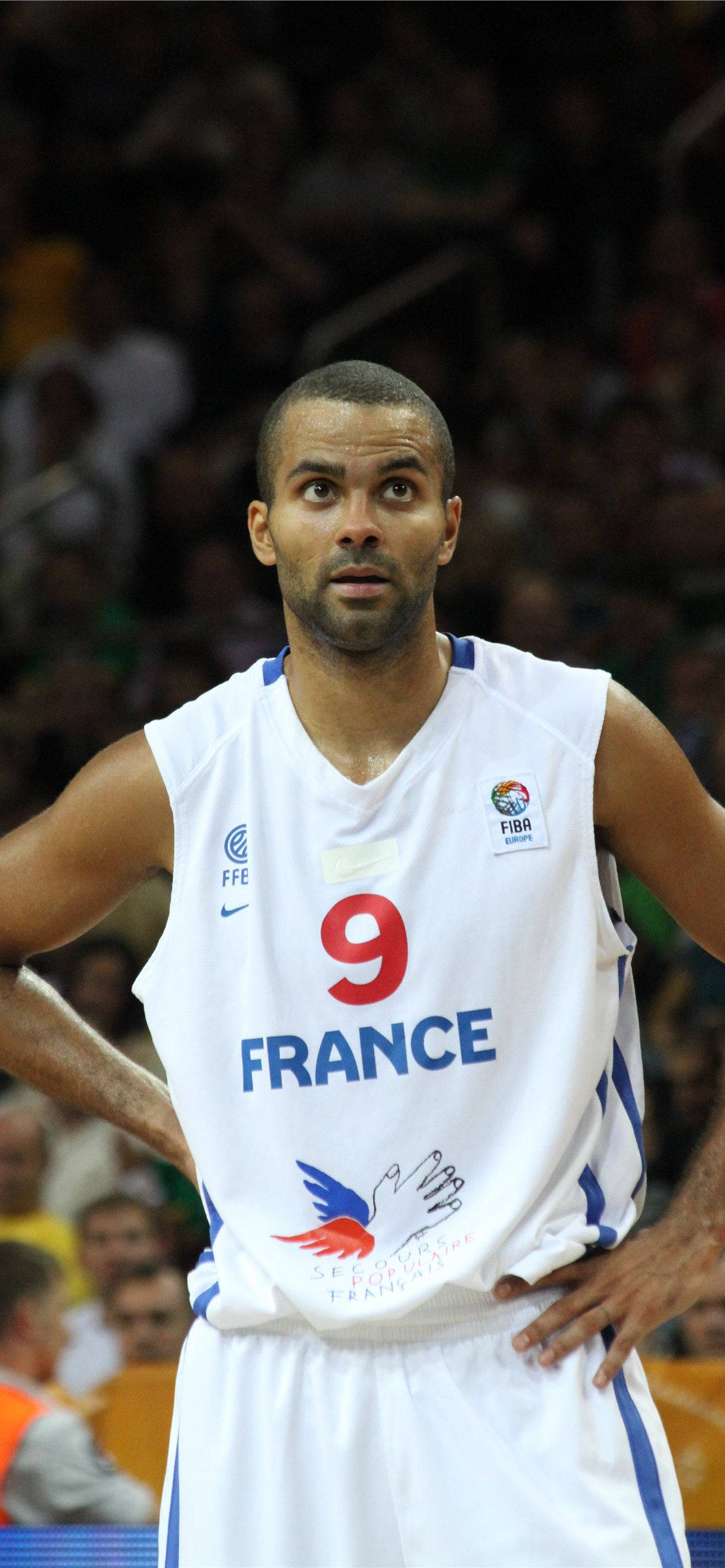 Tony Parker 桌布 壁紙 — 一位專注的法國籃球運動員身穿白色九號球衣，在明亮的場館燈光下比賽期間雙手叉腰站立。