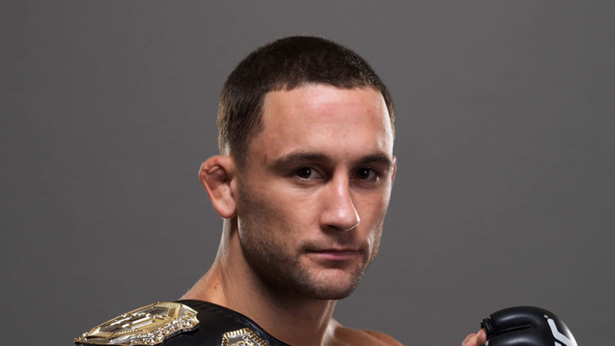 UFC 桌布 壁紙 — 一位專注的混合武術家，帶著冠軍腰帶和拳擊手套，背景為中性灰色。