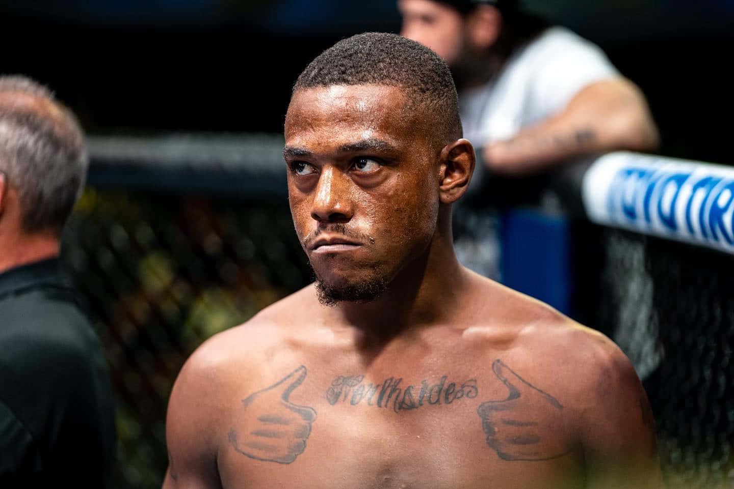 MMA 桌布 壁紙 — 一位專注的混合武術家，胸口有刺青，站在明亮的競技場燈光下的籠子裡。