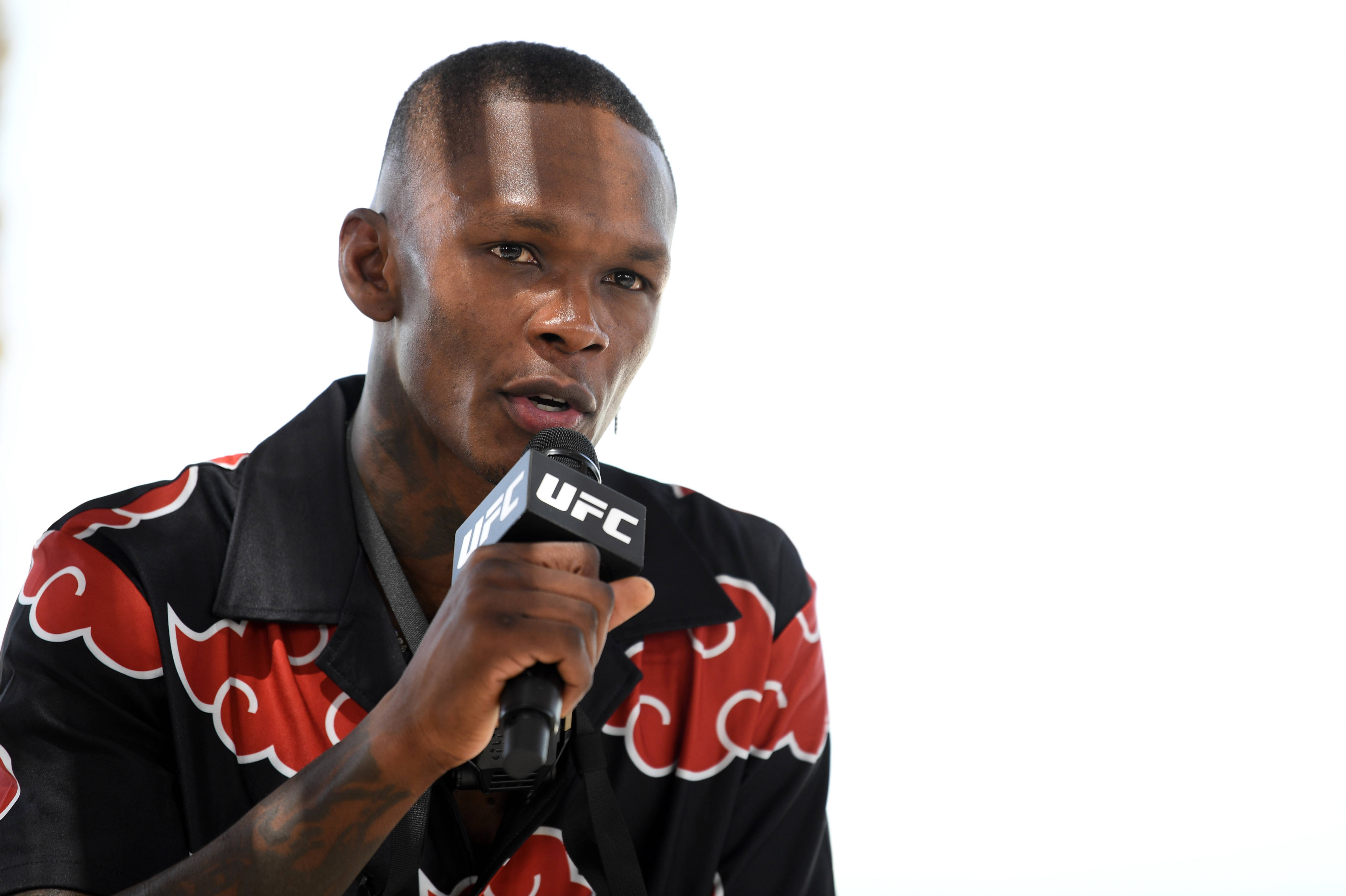 Adesanya 桌布 壁紙 — 一位專注的混合武術家對著UFC麥克風說話，穿著黑色和紅色雲紋襯衫，背景是純白色。