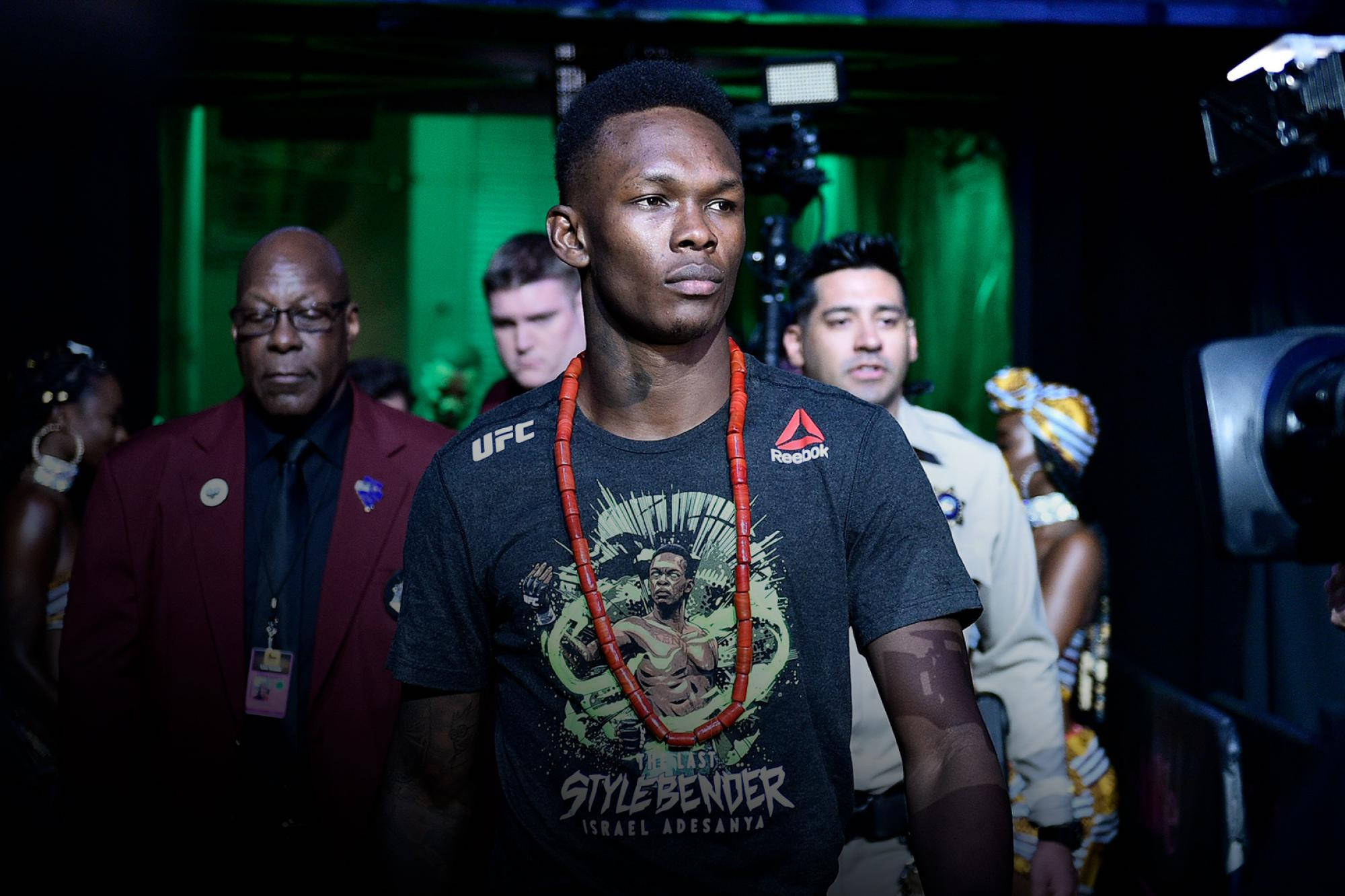 Adesanya 桌布 壁紙 — 一位專注的混合武術家穿著UFC襯衫，在綠色燈光下被相機和保安包圍。