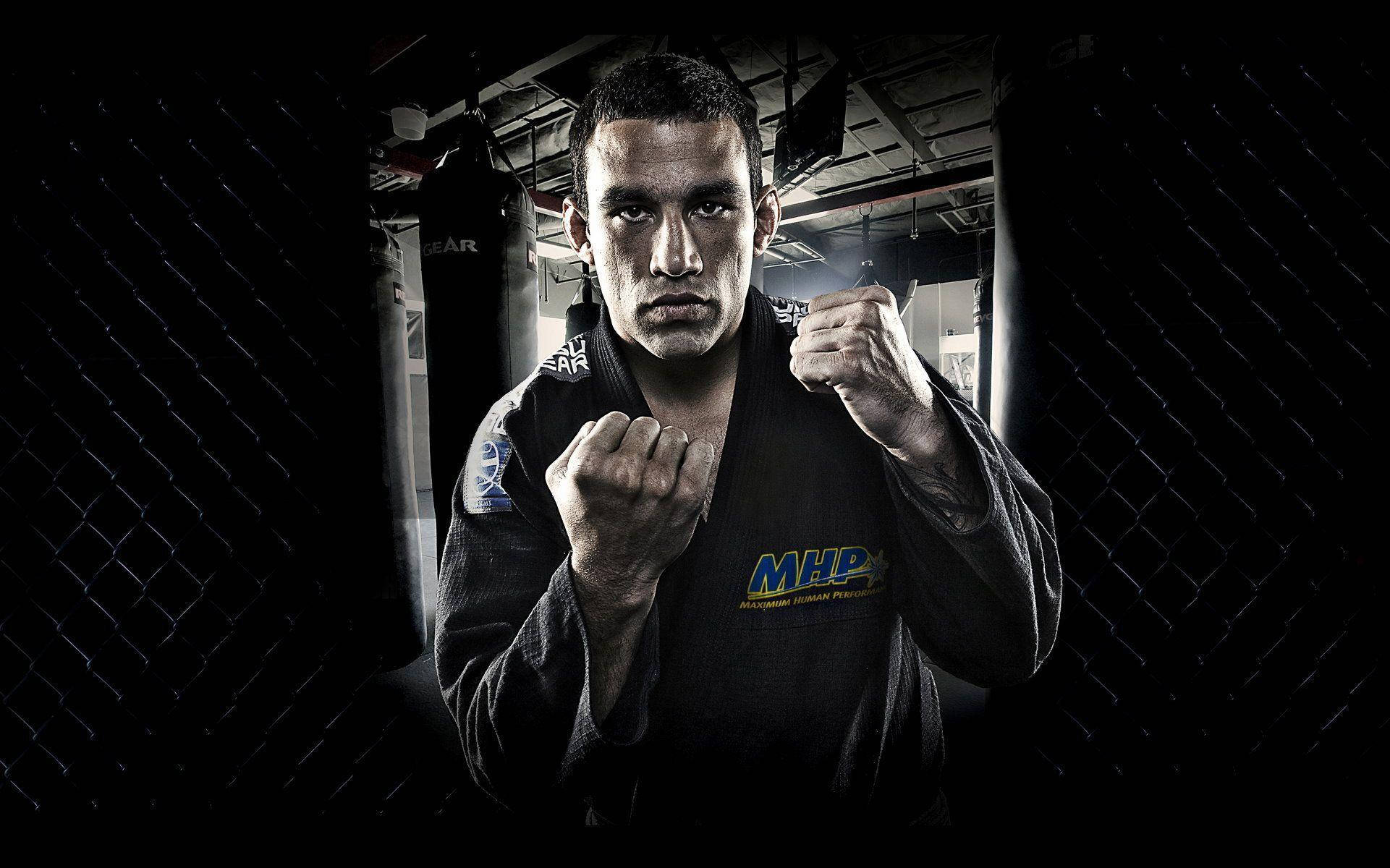 MMA 桌布 壁紙 — 一位專注的混合武術家穿著黑色道服，站在光線昏暗的籠子裡，舉起拳頭準備戰鬥。