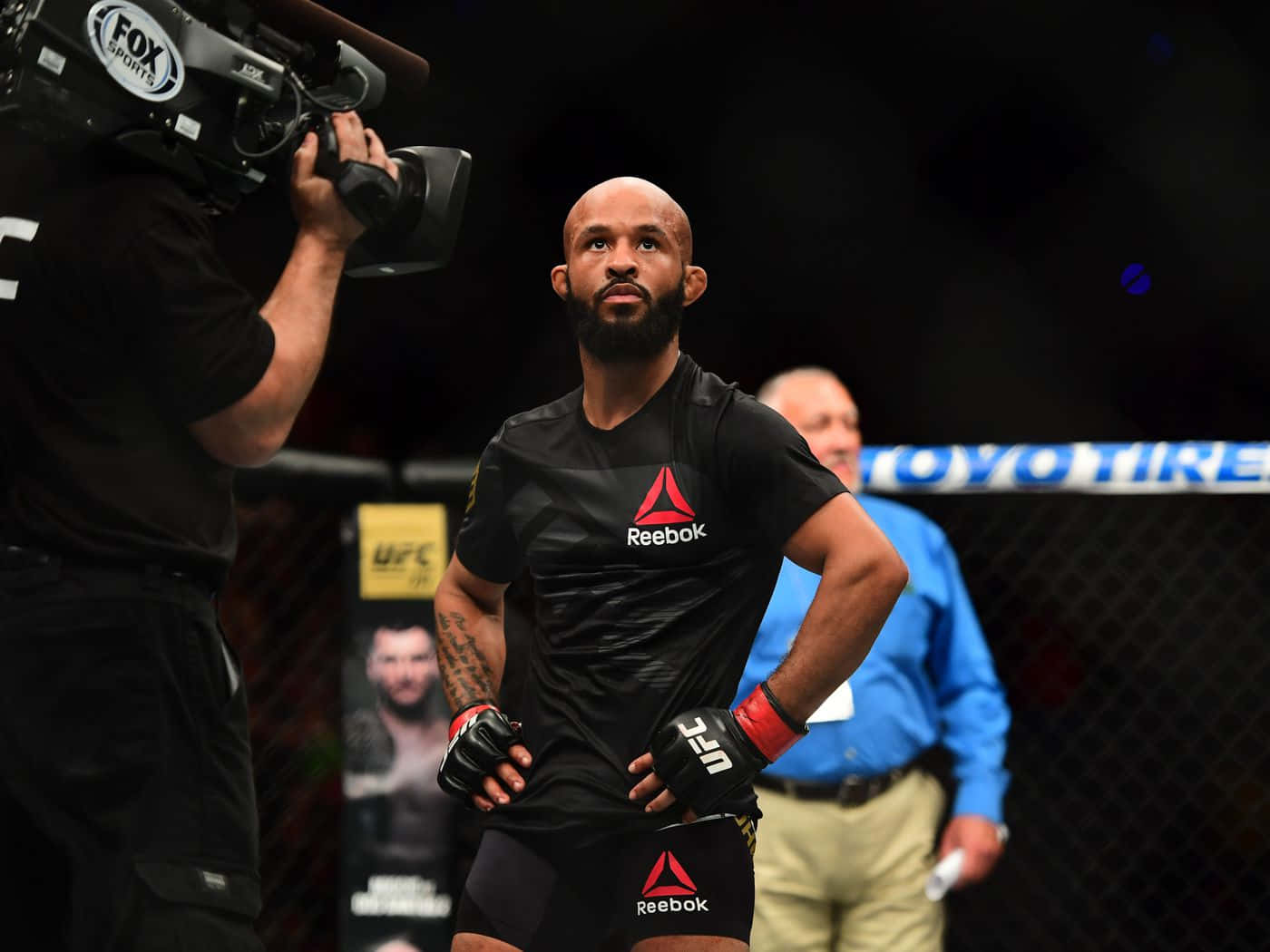 Champion 桌布 壁紙 — 一位專注的混合武術家站在UFC八角籠內，穿著黑色Reebok裝備，帶有紅色點綴，在明亮的場館燈光下。