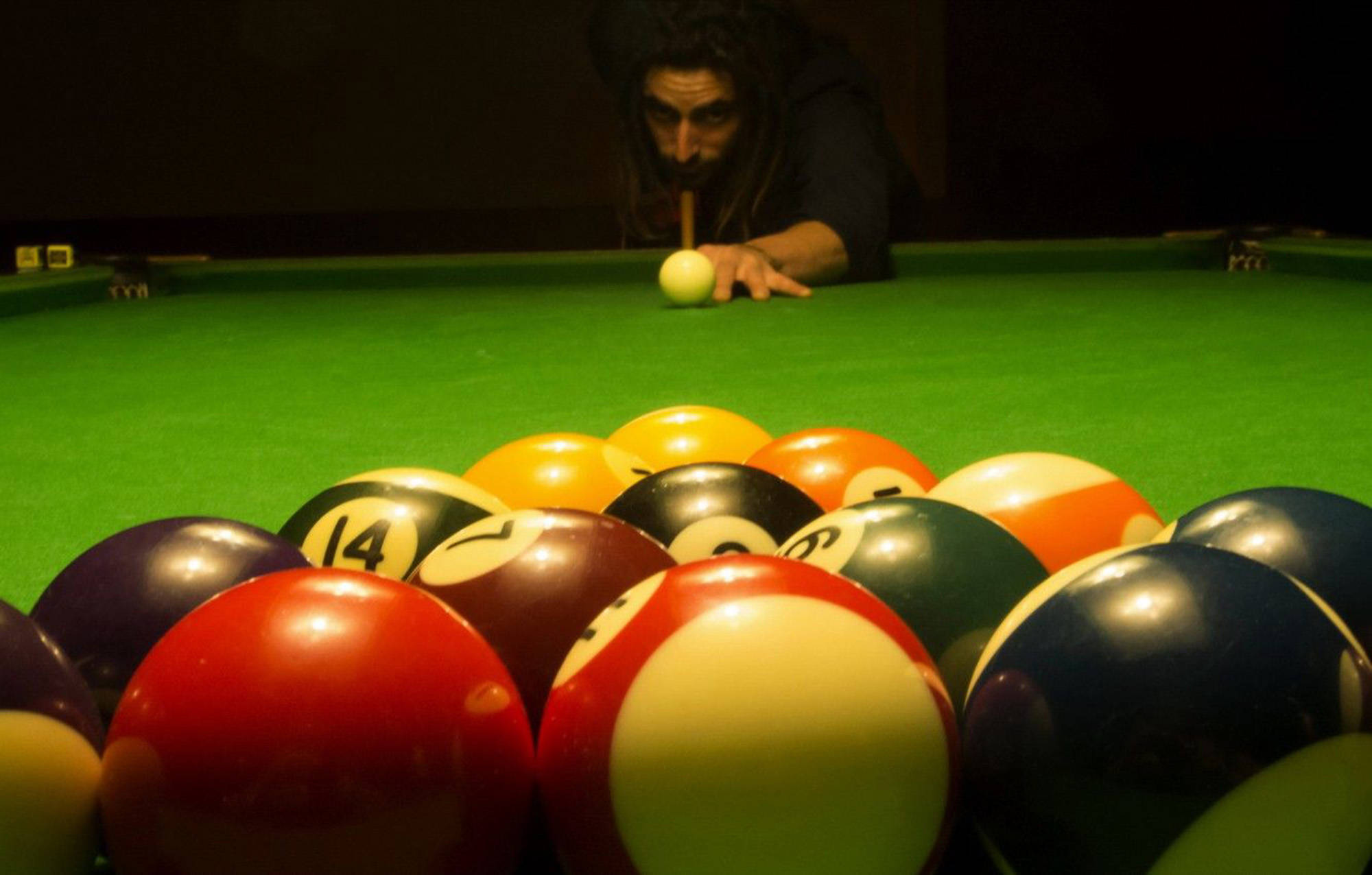 Snooker 桌布 壁紙 — 一位專注的玩家俯身在撞球檯上，瞄準母球，前景有一排色彩繽紛的撞球。