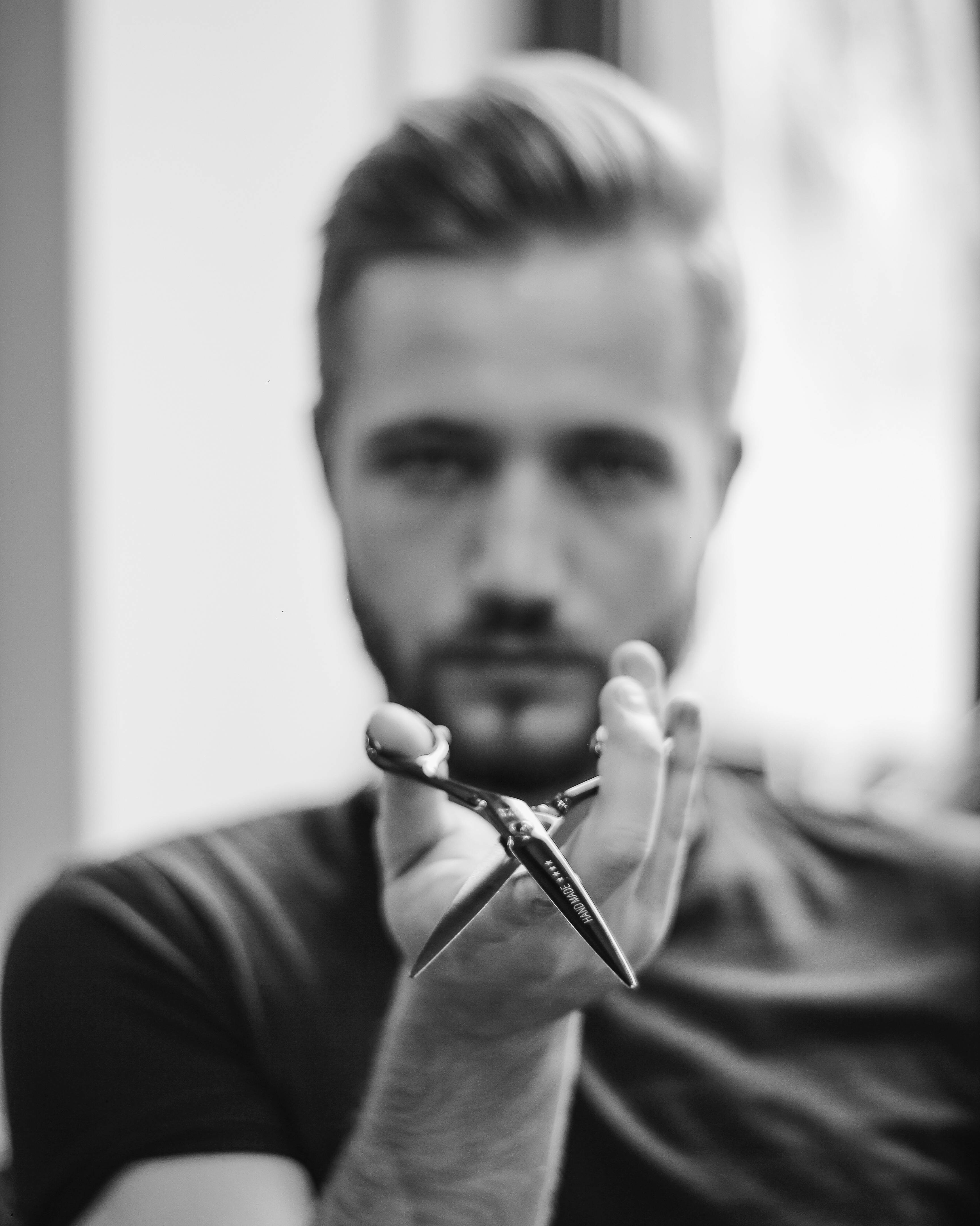 Haircut 桌布 壁紙 — 一位專注的理髮師在前景中拿著鋒利的剪刀，臉部模糊，背景明亮。